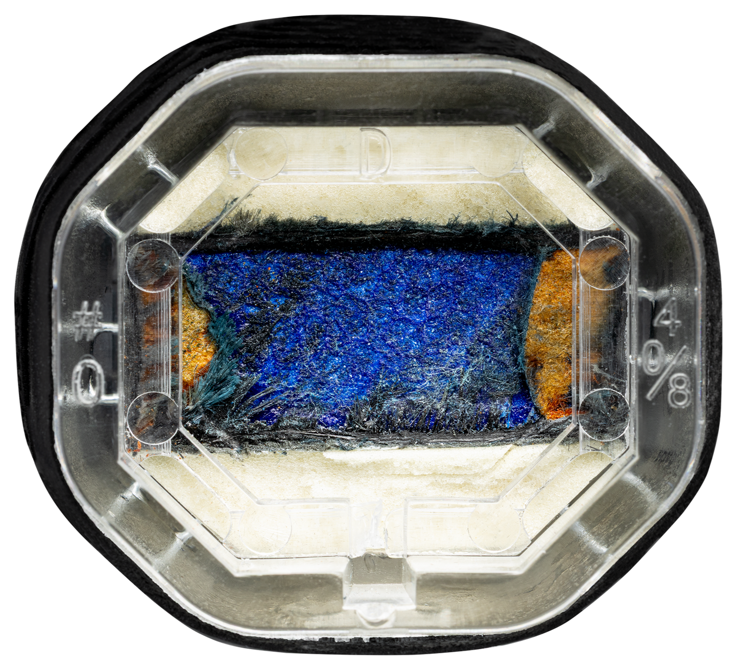 A close-up of a synthetic sapphire wafer in an octagonal, clear plastic holder with black trim, its textured design resembling the layered look found on the Royal Pickleball Diadem ROYAL Warrior BluCore STANDARD 14MM paddle.