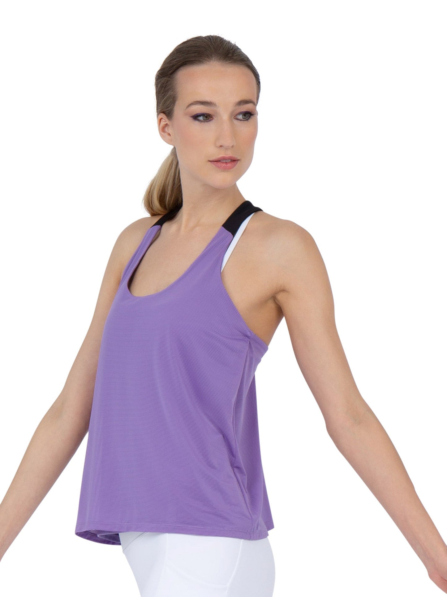 A woman with light skin and straight light brown hair poses against a white background, wearing the inPhorm NYC Double-Layered "T" Racer Back Camila Tank in Lavender/Black over a black sports bra and white leggings.