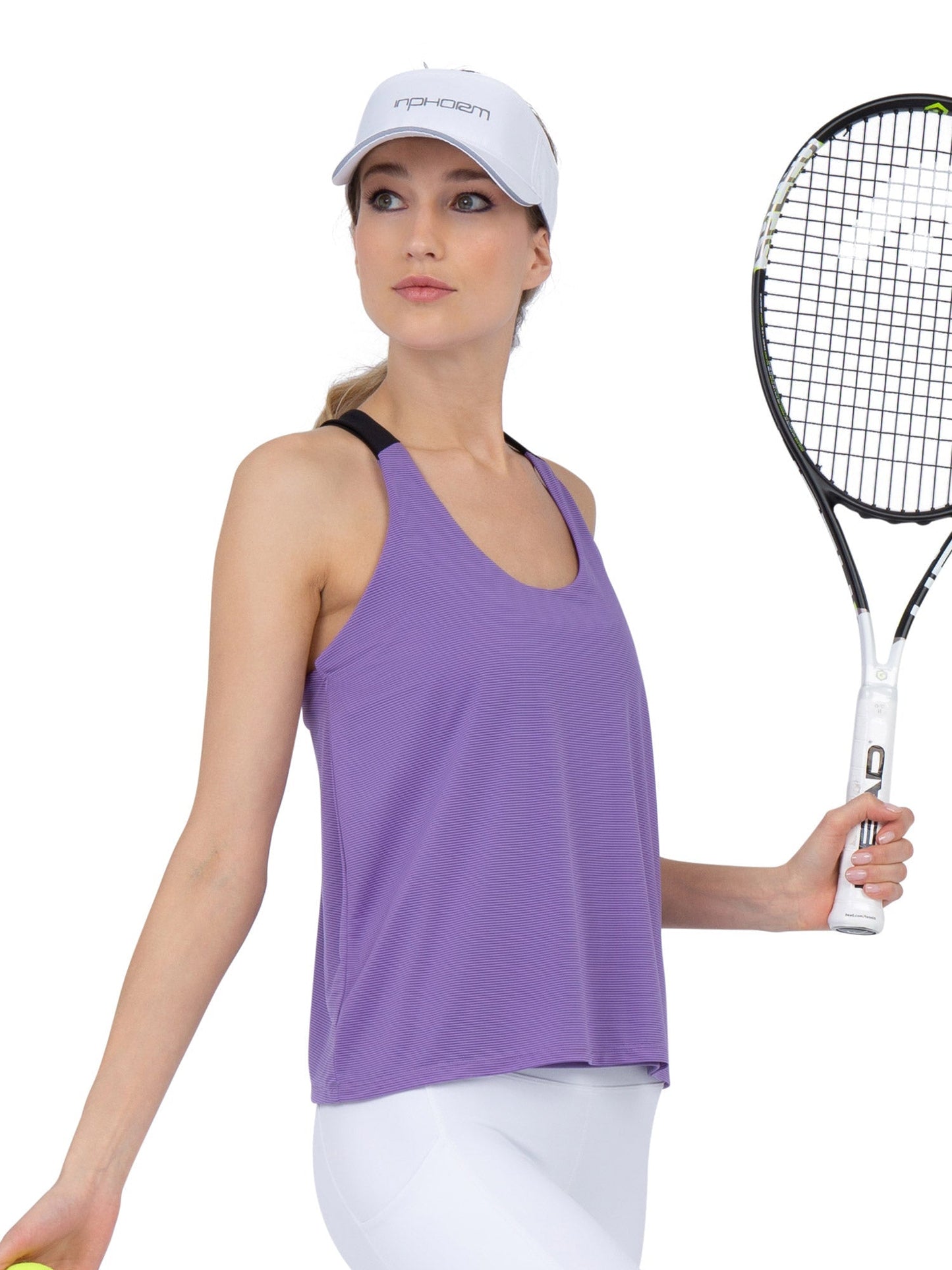 A woman in the inPhorm NYC Double-Layered "T" Racer Back Camila Tank in Lavender/Black, paired with a white cap and leggings, holds a tennis racket and ball, posing confidently against a white background with poise and focus.