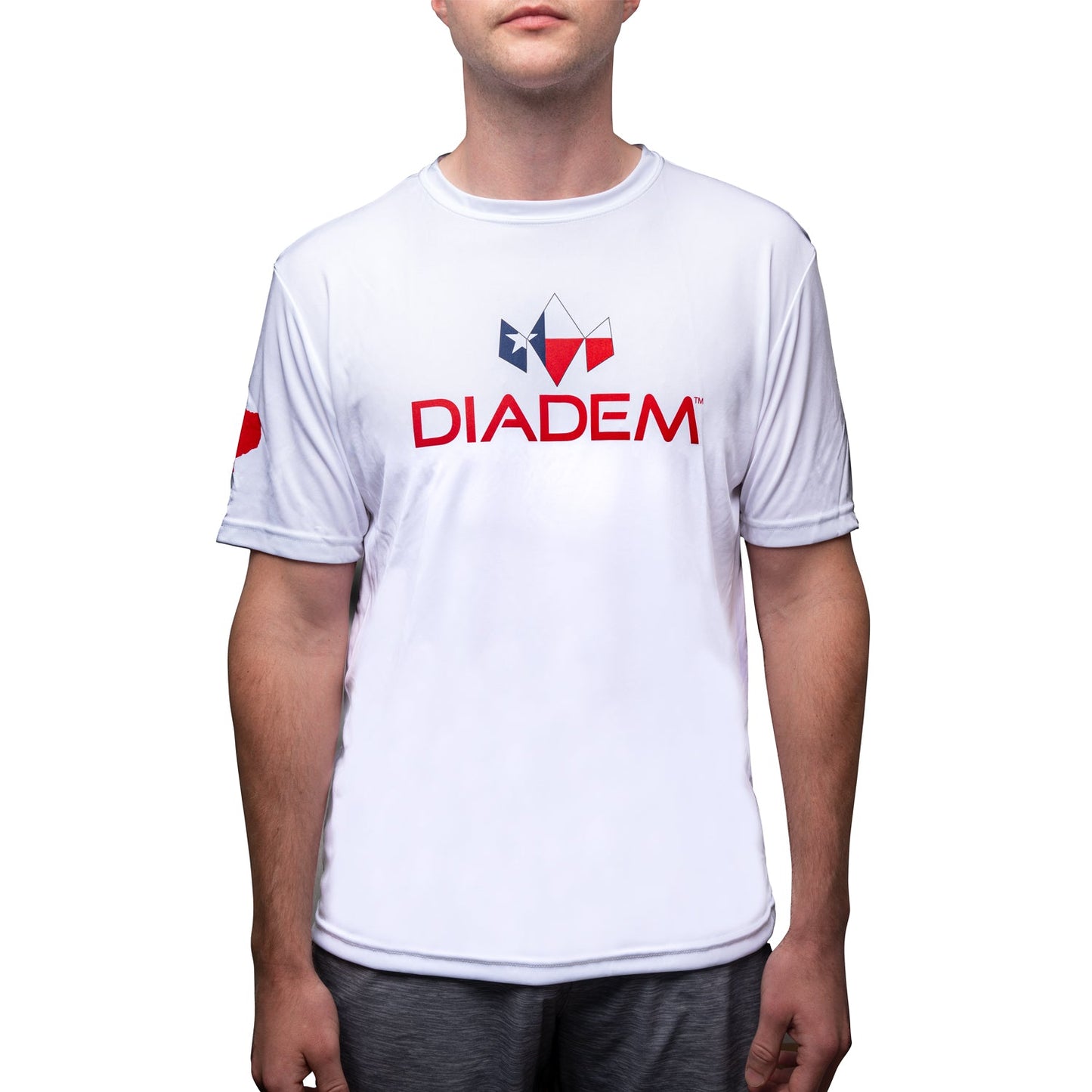 A person wears a white Diadem Sports DryCore T-Shirt Texas Logo with "DIADEM" in red and a blue-red geometric logo above it, plus a sleeve logo. Only the torso and lower face are visible against a white background.
