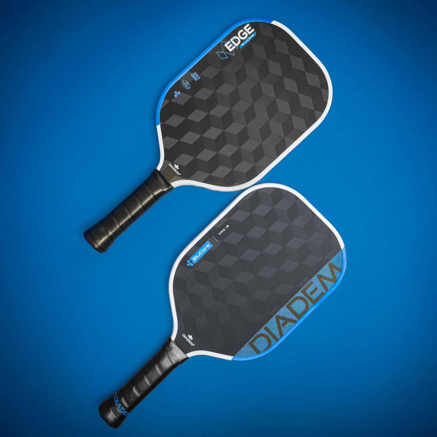 Two USAPA-approved Diadem Sports Edge BluCore Pro paddles with textured hexagonal patterns lie on a blue background. Each has a black wrapped handle and features PowerSync BluCore Technology, with "EDGE" and "DIADEM" shown in bold text.