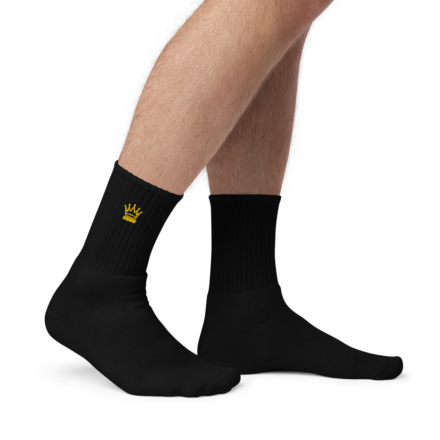 A pair of male legs wear Crown Pickleball's black Embroidered Logo Socks, featuring a cushioned sole and a small yellow crown logo on the ankle. The plain socks stand out against the white background.