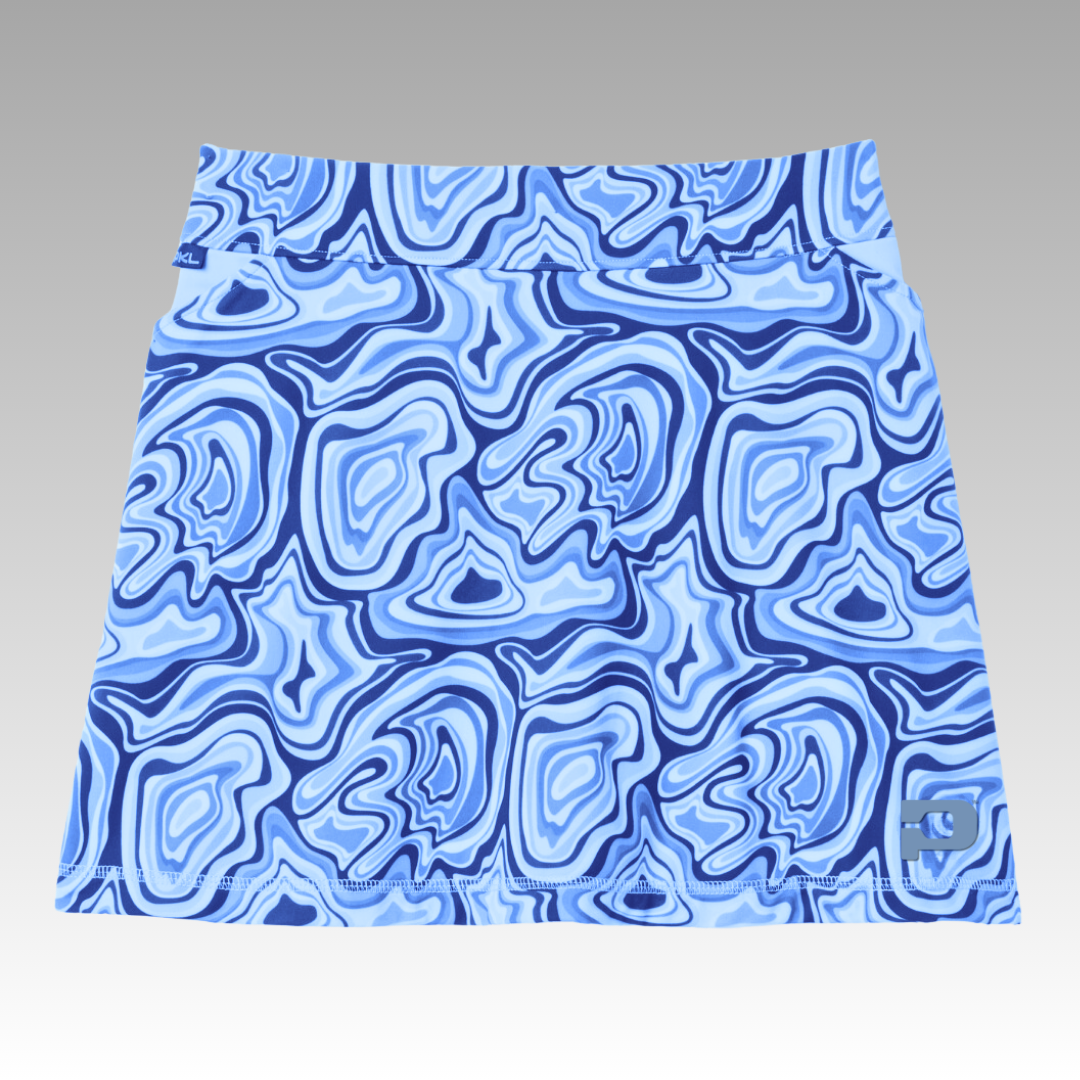 The Playly Store Sammy Skort 2.0 is a blue and light blue pickleball skort with an abstract swirl pattern, crafted from CoolFlow fabric. Details include a small blue tag at the waist and a square logo patch by the bottom right hem.