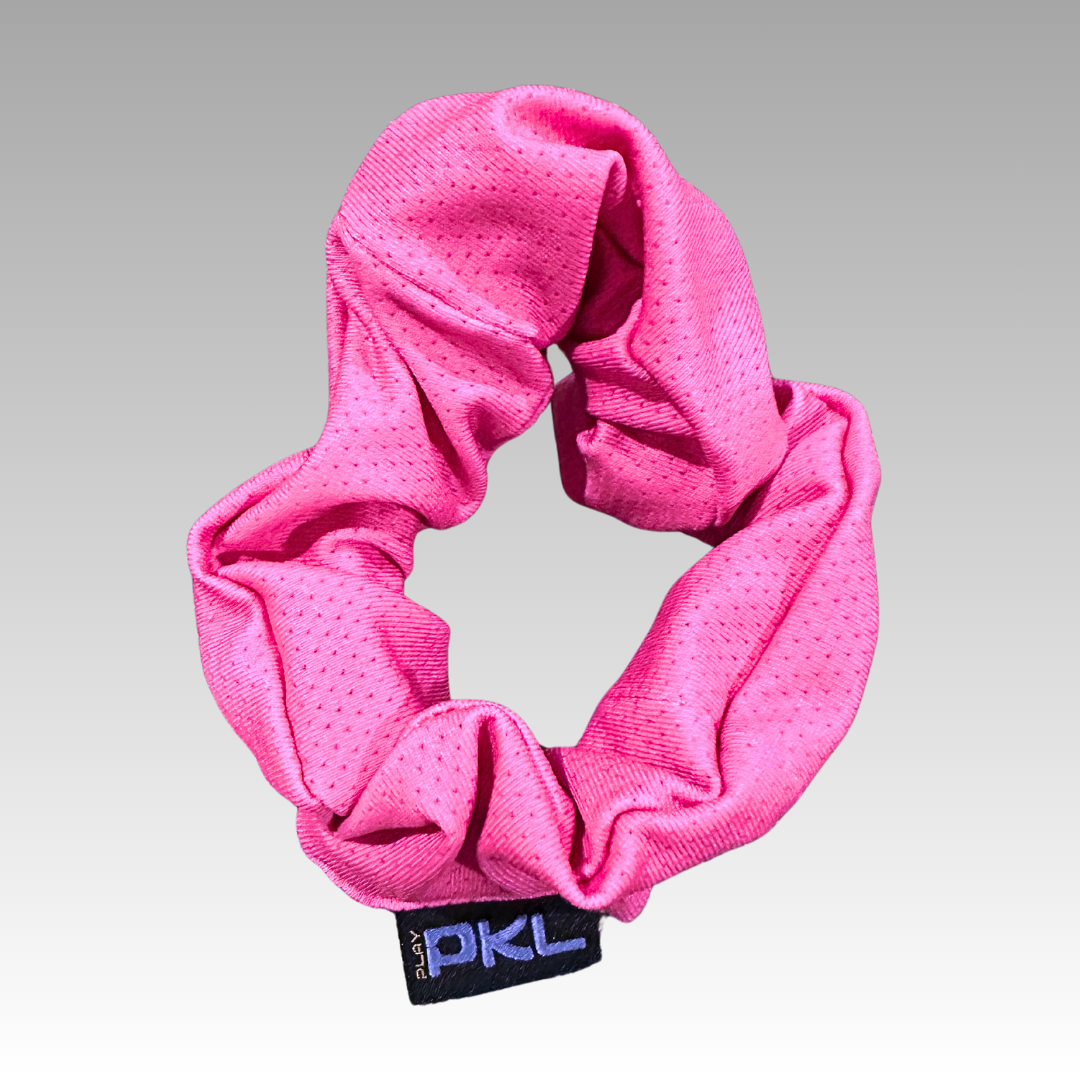 The Shanti Pickleball Hair Scrunchie by Playly Store is a bright pink, textured scrunchie with a subtle wrinkled look and a small black PKL tag, displayed on a gray gradient background.