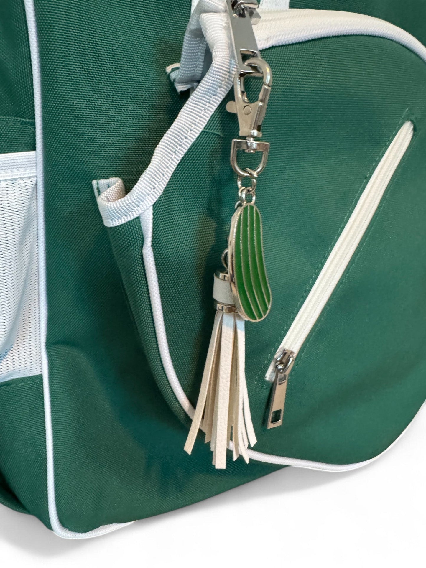 The Fresh Pickle Lola Pickleball Tote Bag is green with white trim and a white front zipper. It comes with a silver clasp keychain featuring a green pickle charm and beige leather fringe tassels—ideal for pickleball fans.