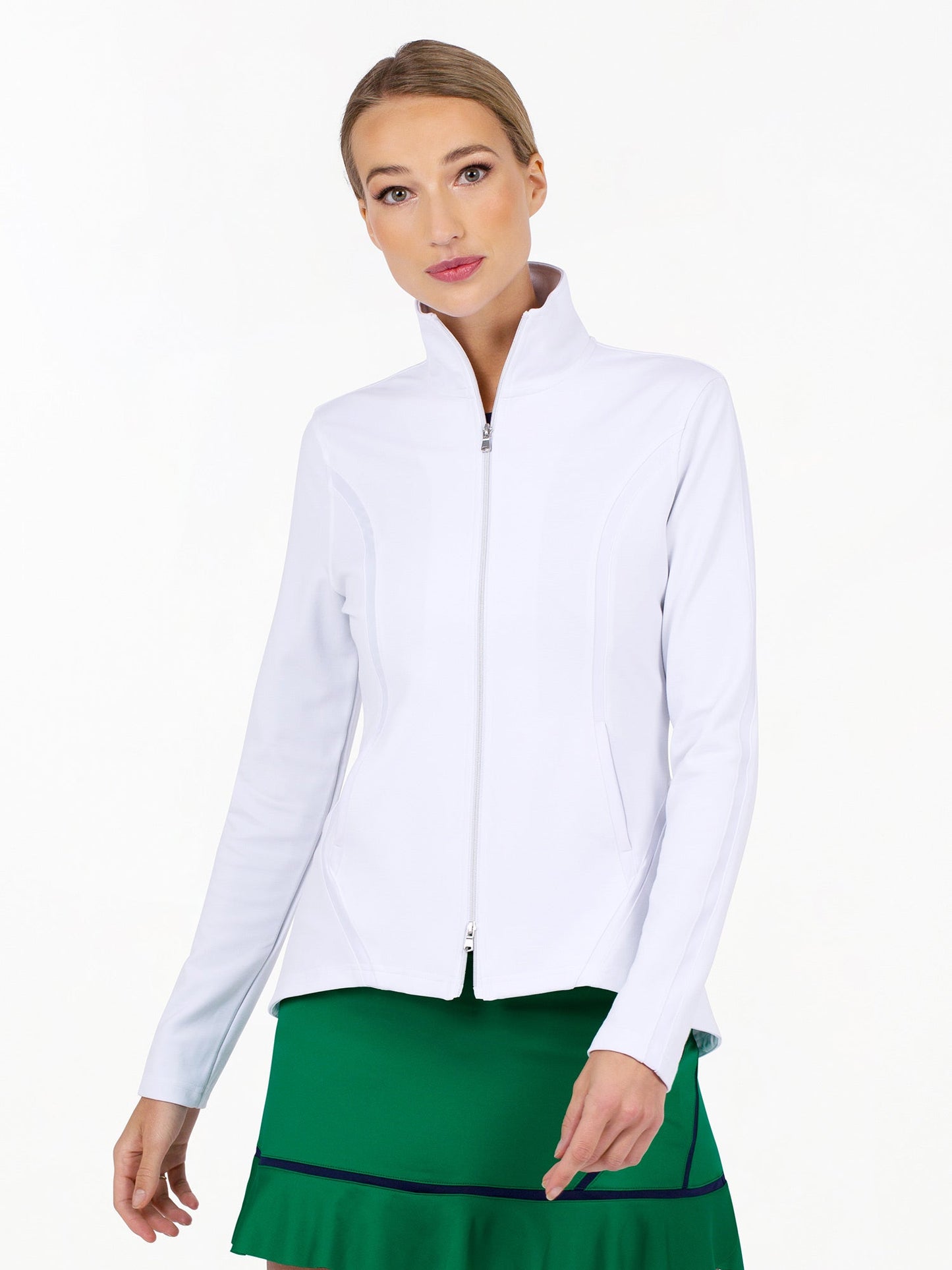 A light-skinned, blonde-haired woman wears the inPhorm NYC Harlow Knit Jacket in white, a zip-up with a high collar, paired with a green skirt with navy trim. She stands against a plain white background, gazing slightly to the side.