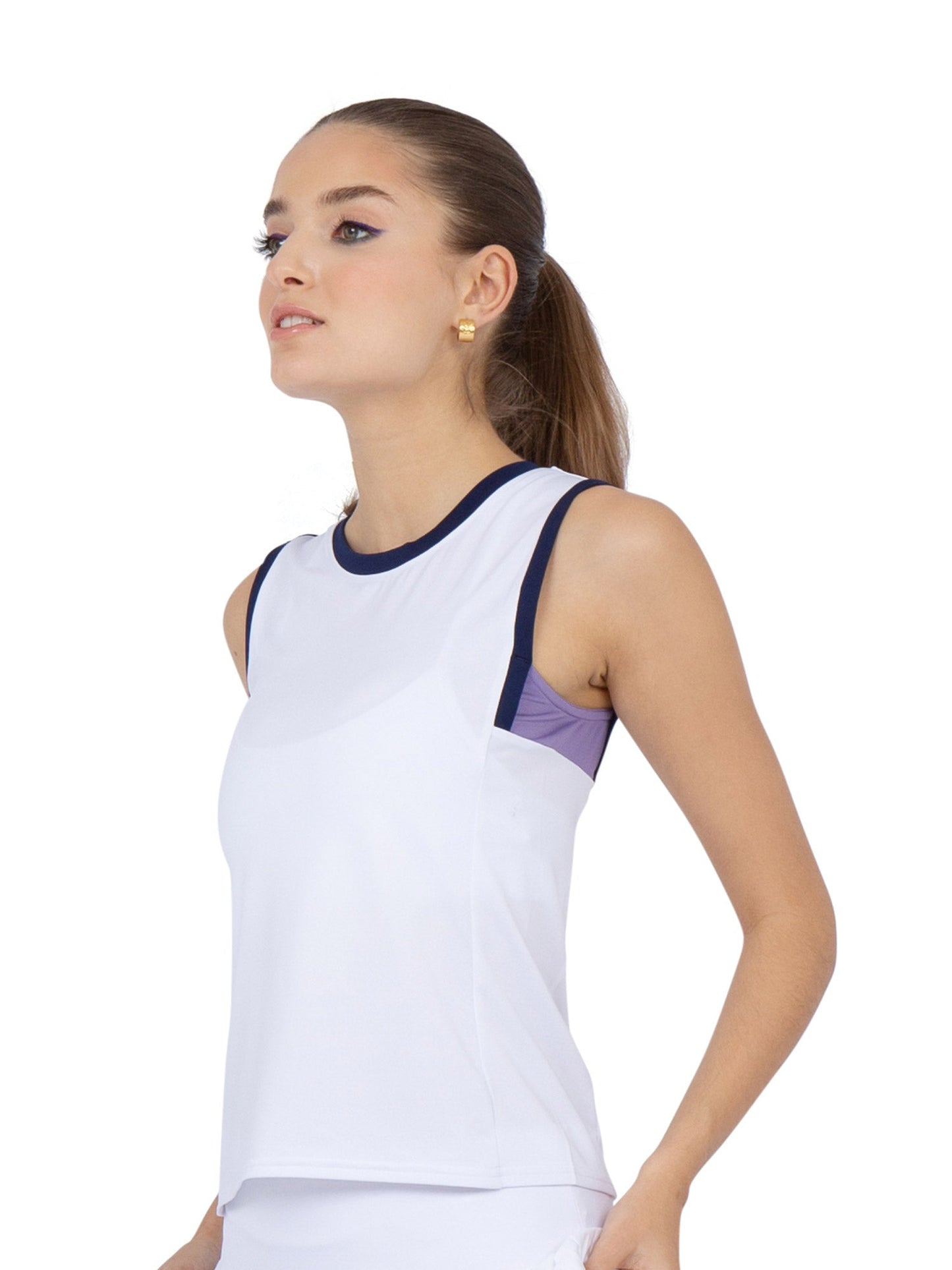 A young woman with light skin and brown hair tied back wears the inPhorm NYC Harper Performance Tank in White/Lavender Combo, standing in semi-profile and looking upward to showcase the tank’s moisture-wicking fabric.
