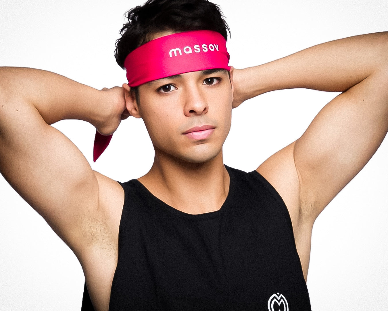 A young man wearing a black sleeveless shirt and the Massov Headband Tie in pink stands with arms raised and hands behind his head, looking calmly at the camera against a plain white background.