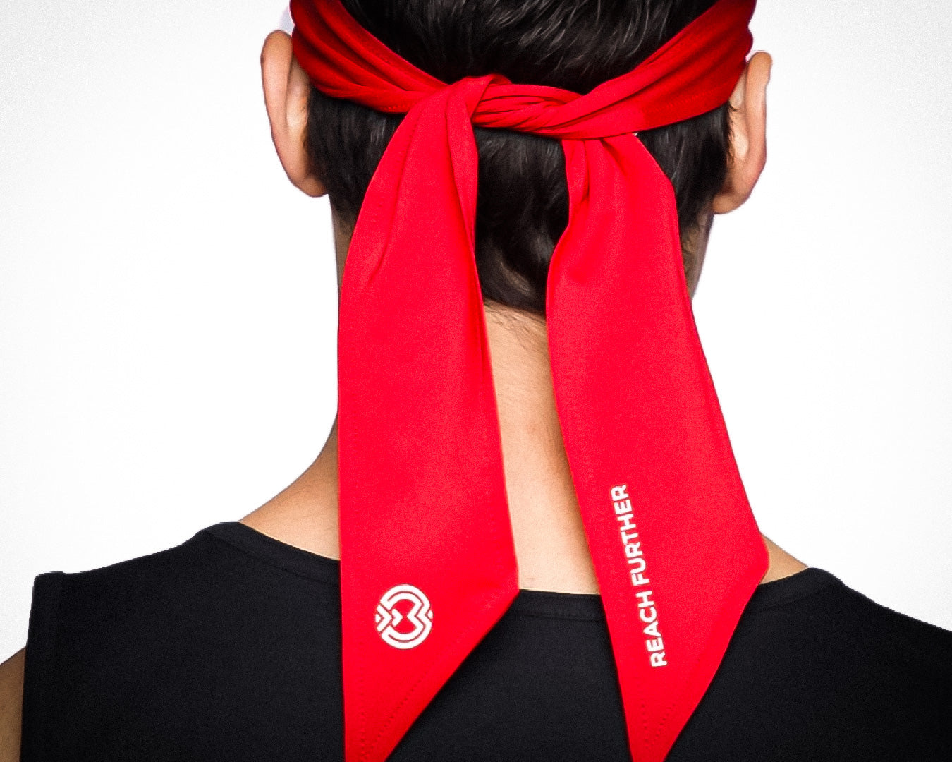 A person in a sleeveless black shirt is shown from behind wearing a red Massov Headband Tie, sweat-wicking with “REACH FURTHER” in white text and a white circular logo on one end.