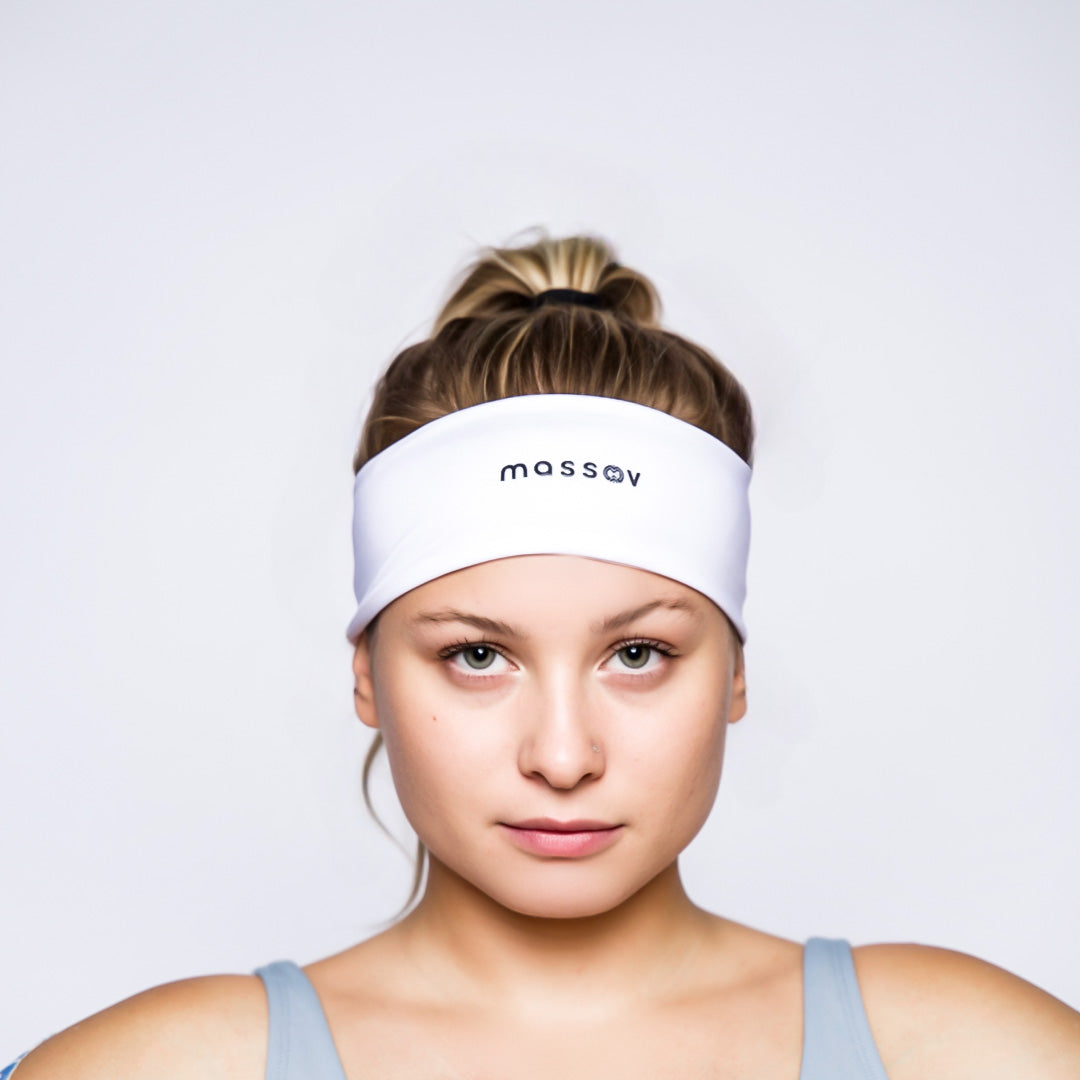 A light-skinned woman with blonde hair tied back wears a white Massov Headband Tie with "massov" in black letters. She pairs it with a light blue tank top and faces the camera against a plain white background, neutral expression.