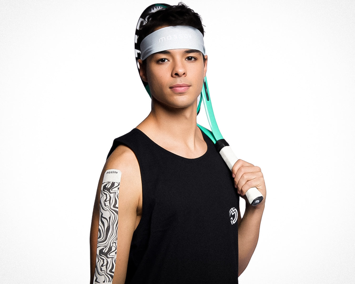 A young person wears a Massov Headband Tie and a black sleeveless shirt, holding a green and black tennis racket over their shoulder. They display a confident look against a plain white background, with an abstract patch on their upper arm.
