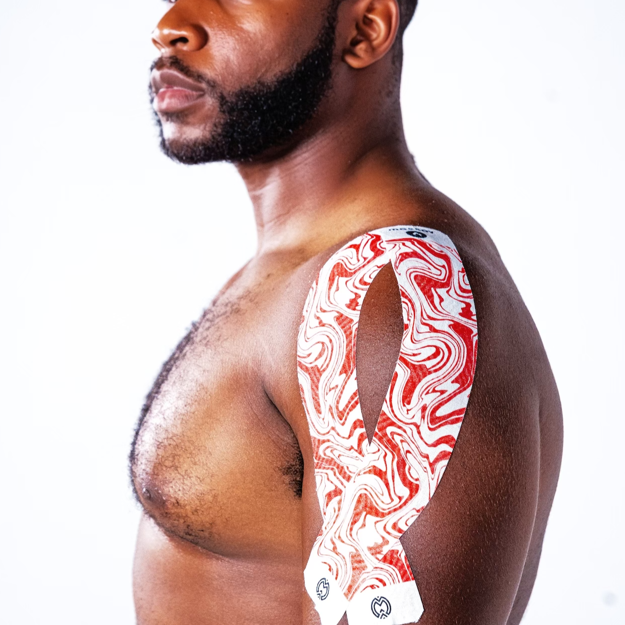 A man with a trimmed beard faces left, displaying his bare upper torso. Red and white Massov Heat Therapy Kinesiology Tape is applied from his shoulder down his upper arm against a plain white background.