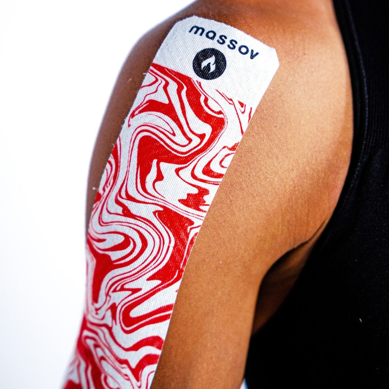 A person’s upper arm is wrapped with Massov Heat Therapy Kinesiology Tape, featuring bold red swirls. They wear a black sleeveless shirt, set against a bright minimal background to highlight this muscle pain relief solution.