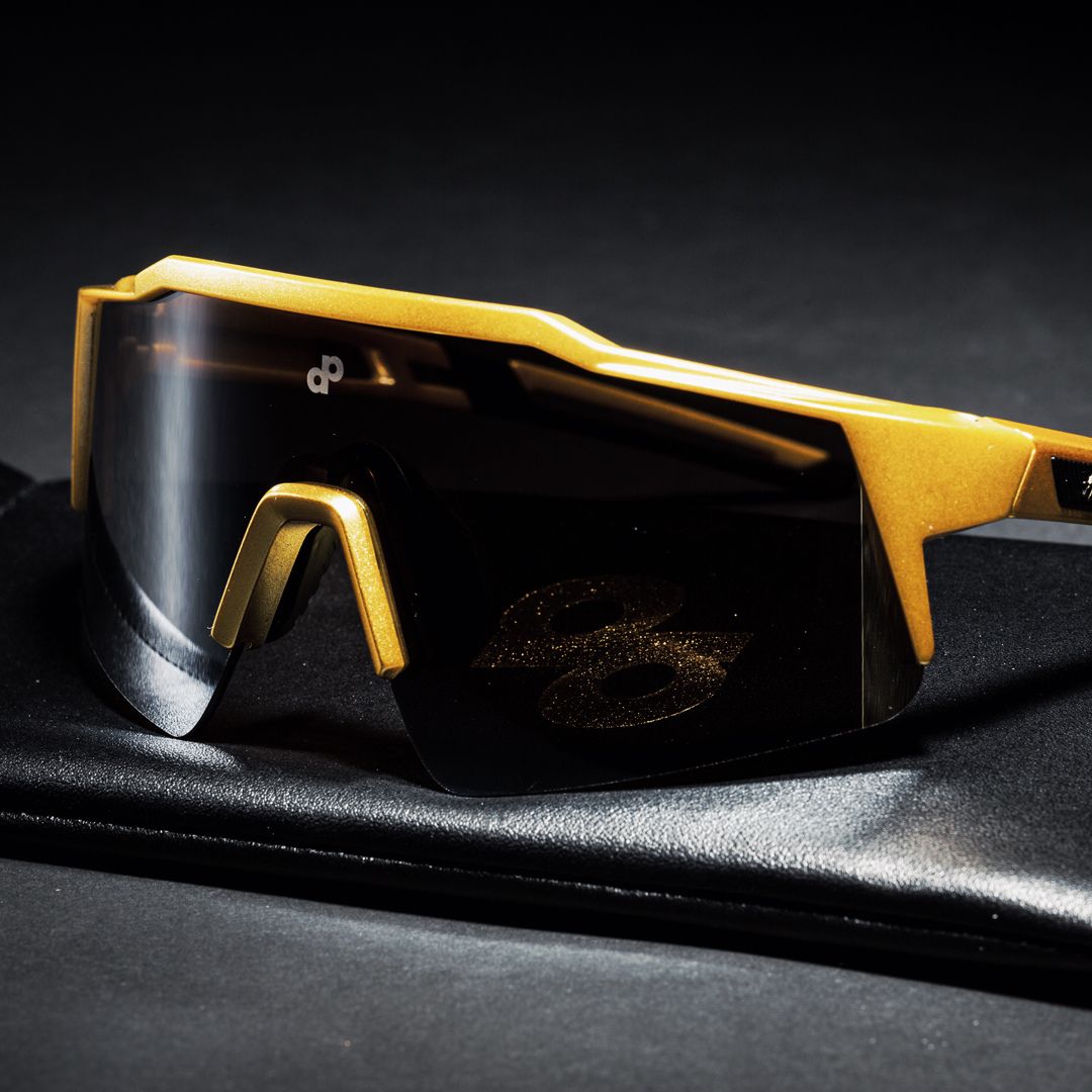 A close-up of Dope Pickleball Co. High Roller Performance Pickleball Sunglasses with a yellow-gold frame and large dark lenses rests on a black leather case, the “dp” logo highlighting these sleek pickleball sunglasses.