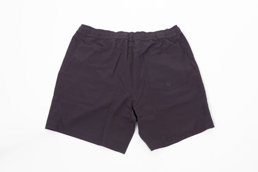 The Thrive Pickleball Thrive Elite Shorts (7 in.) are dark purple, quick-drying shorts with an elastic waistband, two side seams, and a right back pocket. Made from lightweight recycled fabric and shown laid flat on a white background.