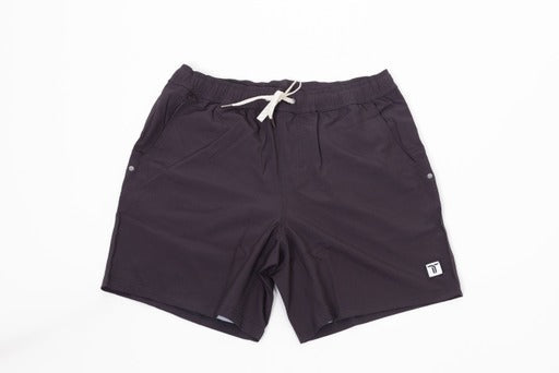 The Thrive Elite Shorts (7 in.) by Thrive Pickleball are black lightweight stretch shorts with an elastic waistband, white drawstring, side pockets, and a small rectangular logo patch on the lower left leg. Laid flat on a white background.