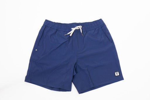 The Thrive Elite Shorts (7 in.) by Thrive Pickleball are blue, quick-drying shorts with an elastic waistband, white drawstring, and a small white and black logo patch on the lower left leg, shown laid flat on a white background.