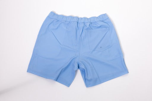 The Thrive Pickleball Elite Shorts (7 in.) in light blue are shown laid flat on a white background, highlighting their lightweight, quick-drying fabric, elastic waistband, and a back patch pocket with drainage grommet.