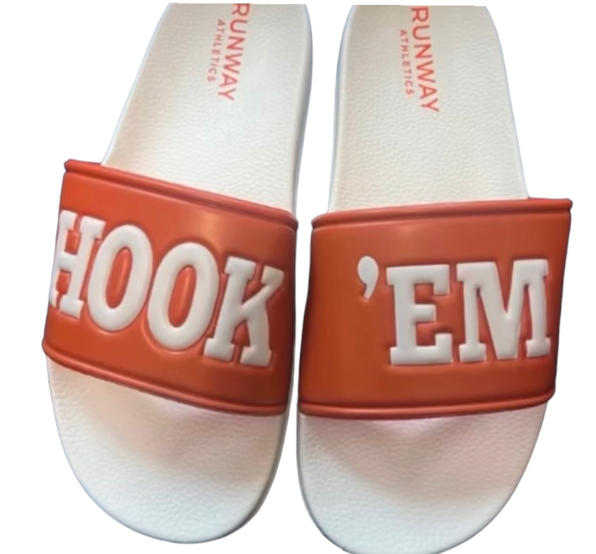 The HOOK 'EM Slides - LIMITED EDITION by Runway Athletics are white sandals with bold orange straps. "HOOK" appears on the left, "EM" on the right, and RUNWAY ATHLETICS is embossed on the footbed for a premium touch.