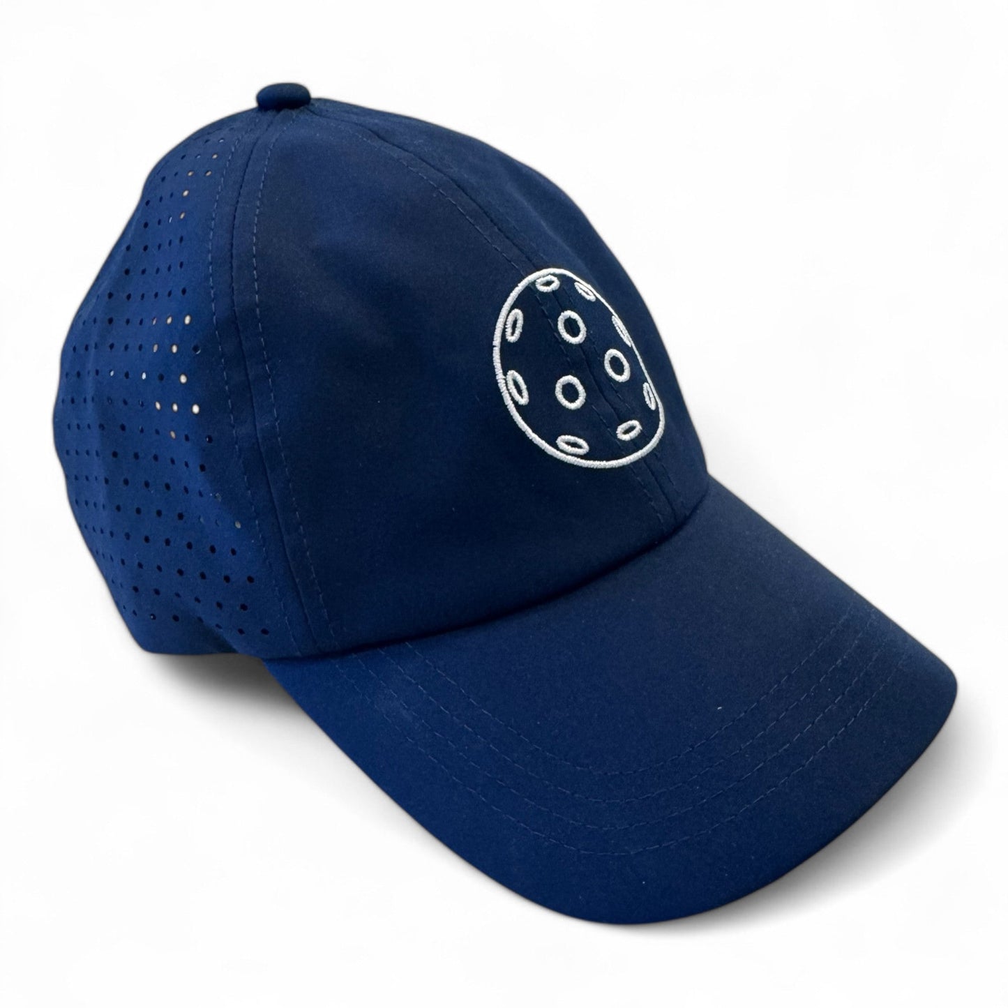 The Fresh Pickle Pickleball Cap is a dark blue, breathable sports cap with side ventilation holes and a white embroidered logo— a stylized circle with six ovals—on the front. Displayed on a white background.