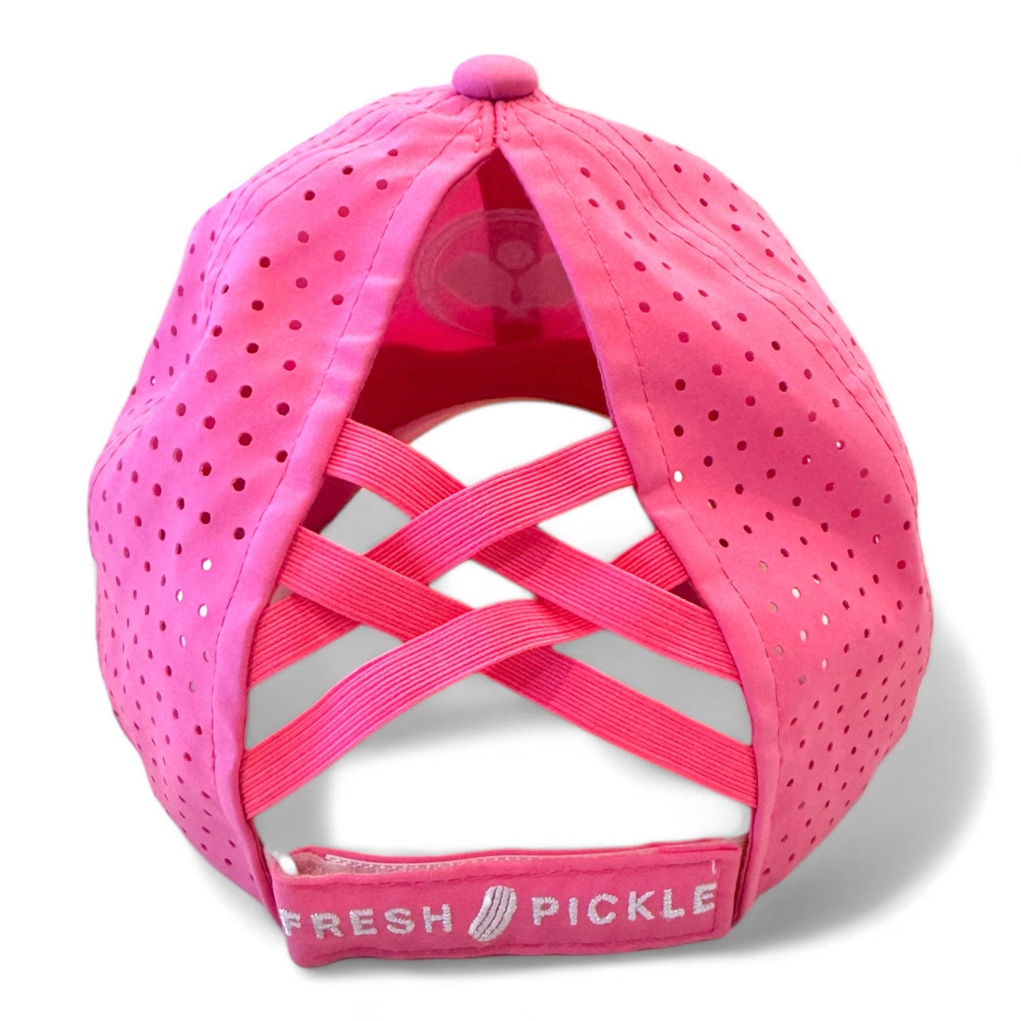 The Fresh Pickle Pickleball Cap is bright pink with crisscrossed elastic bands and ventilation holes at the back. An adjustable strap displays “FRESH PICKLE” and a pickle icon, plus a matching pink top button.