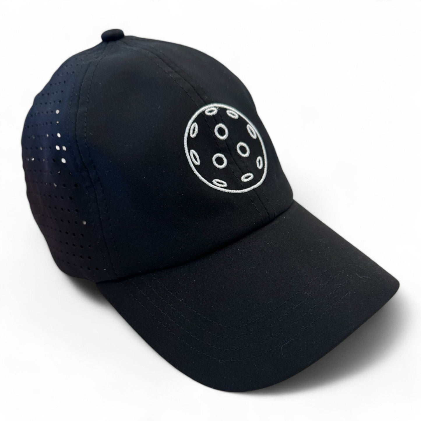 The Fresh Pickle Pickleball Cap is a black, breathable sports cap with side ventilation holes and an embroidered white circle design on the front. It's displayed on a white background.