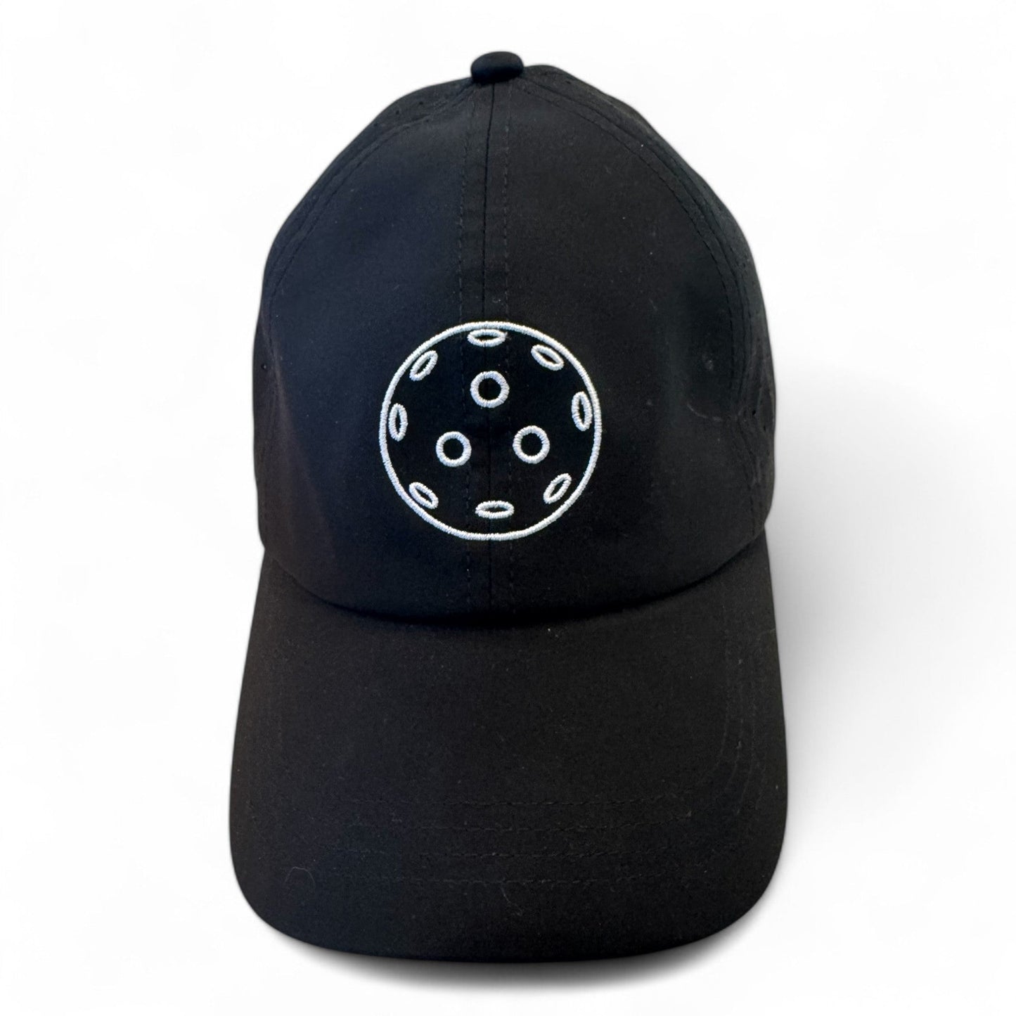 The Fresh Pickle Pickleball Cap features a black design with a white embroidered circle of six dots around a center dot. This breathable sports cap is perfect for stylish, active wear and is shown against a plain white background.