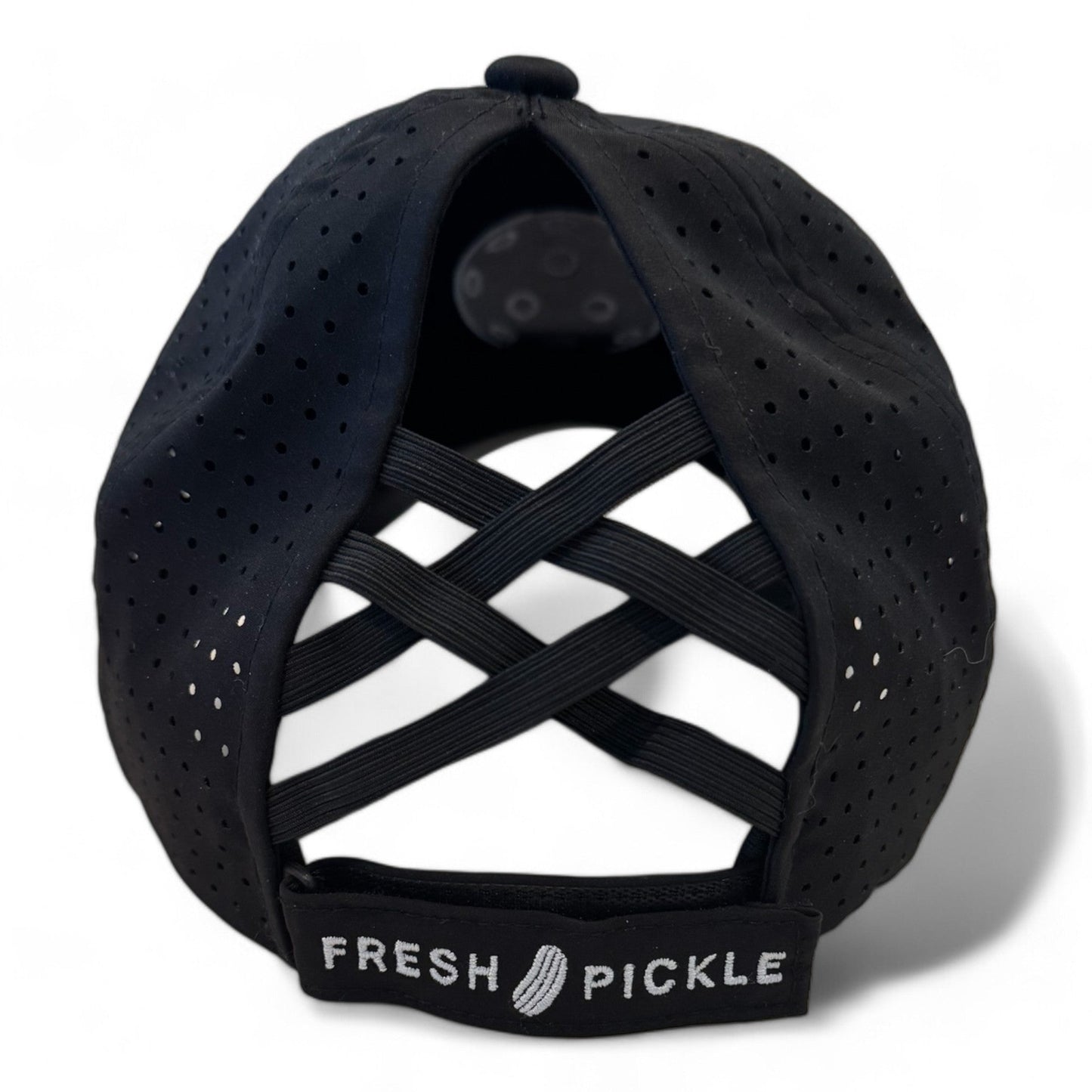 A black perforated Pickleball Cap by Fresh Pickle, viewed from the back, with crisscrossed elastic bands and an adjustable strap featuring "FRESH PICKLE" and a small pickle graphic—perfect for women who play pickleball.