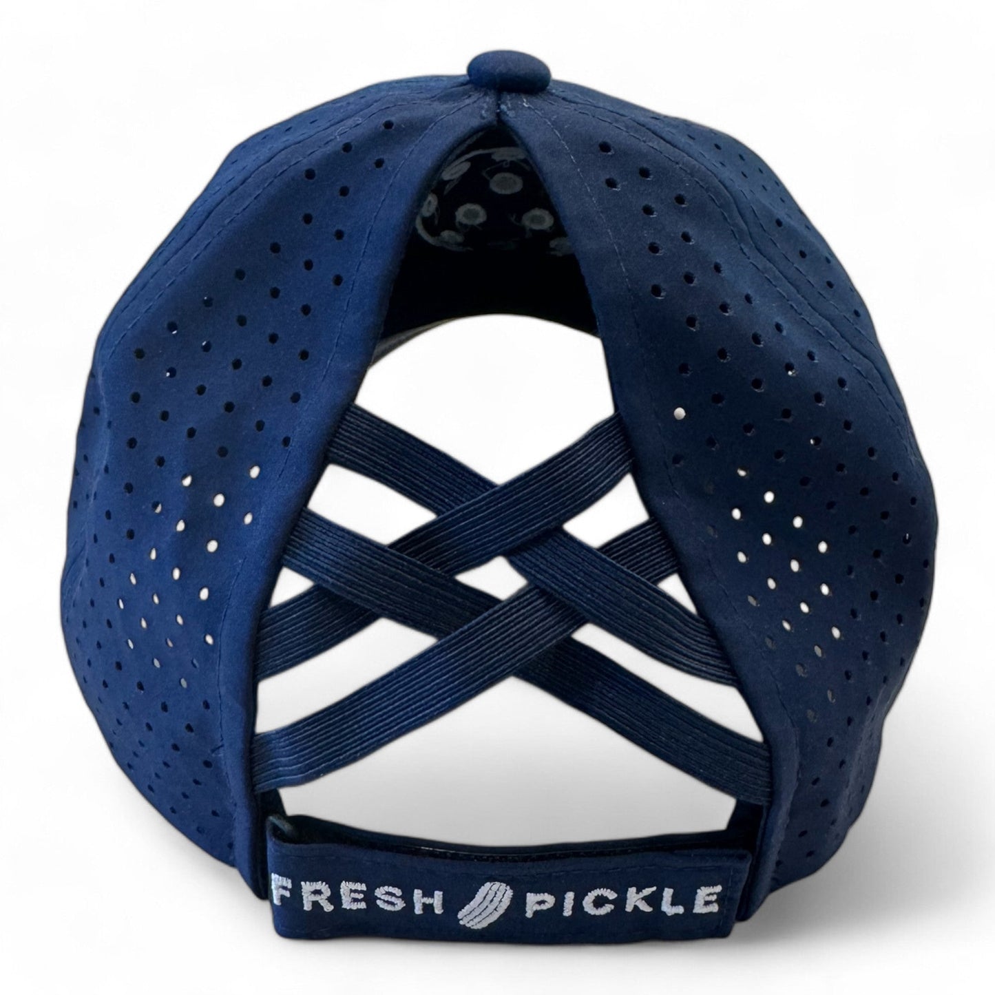 A navy blue Fresh Pickle women's pickleball cap viewed from the back, featuring ventilation holes, two crisscrossed elastic bands above the opening, and an adjustable strap embroidered with “FRESH PICKLE” and a pickle graphic.