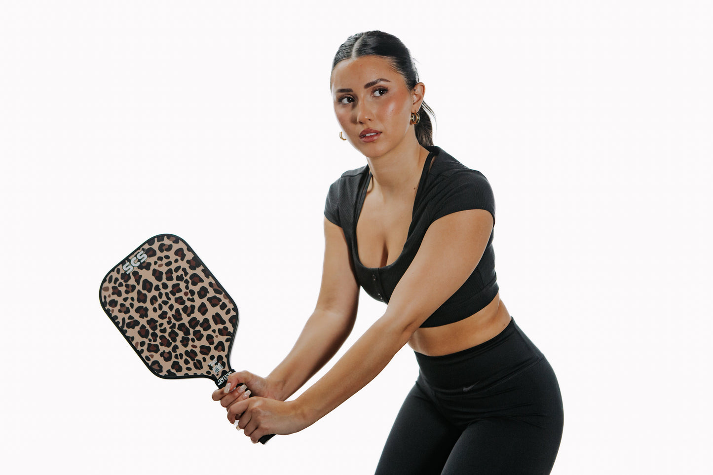 A woman in black athletic wear holds the Salted City Sports Leopard | Evo-Lite Series Pickleball Paddle, ready to play with a focused expression against a plain white background. USA Pickleball Approved.