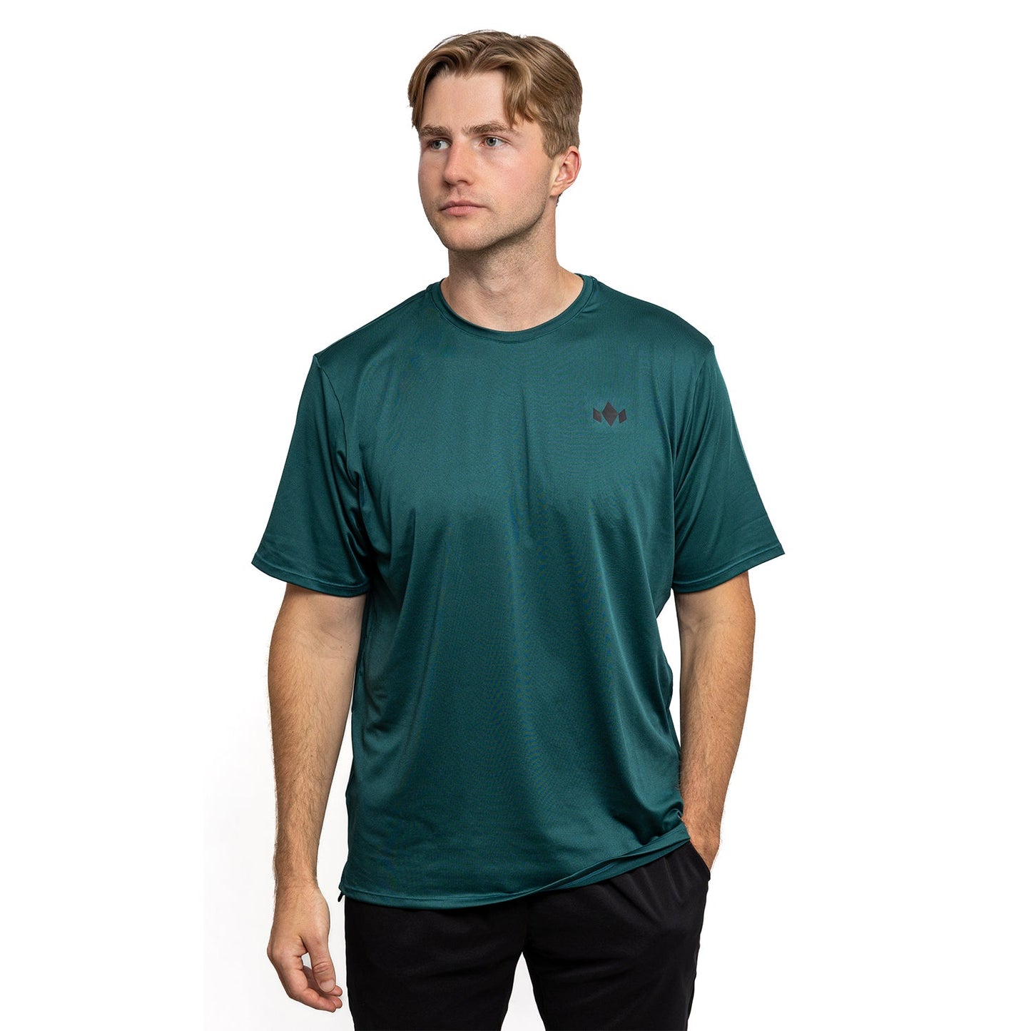 A young man with light brown hair wears the Diadem Sports Men's Essential Crew Neck, a teal-green fast-drying athletic shirt with a black chest logo, paired with black pants. He stands against a white background looking slightly right, expression neutral.
