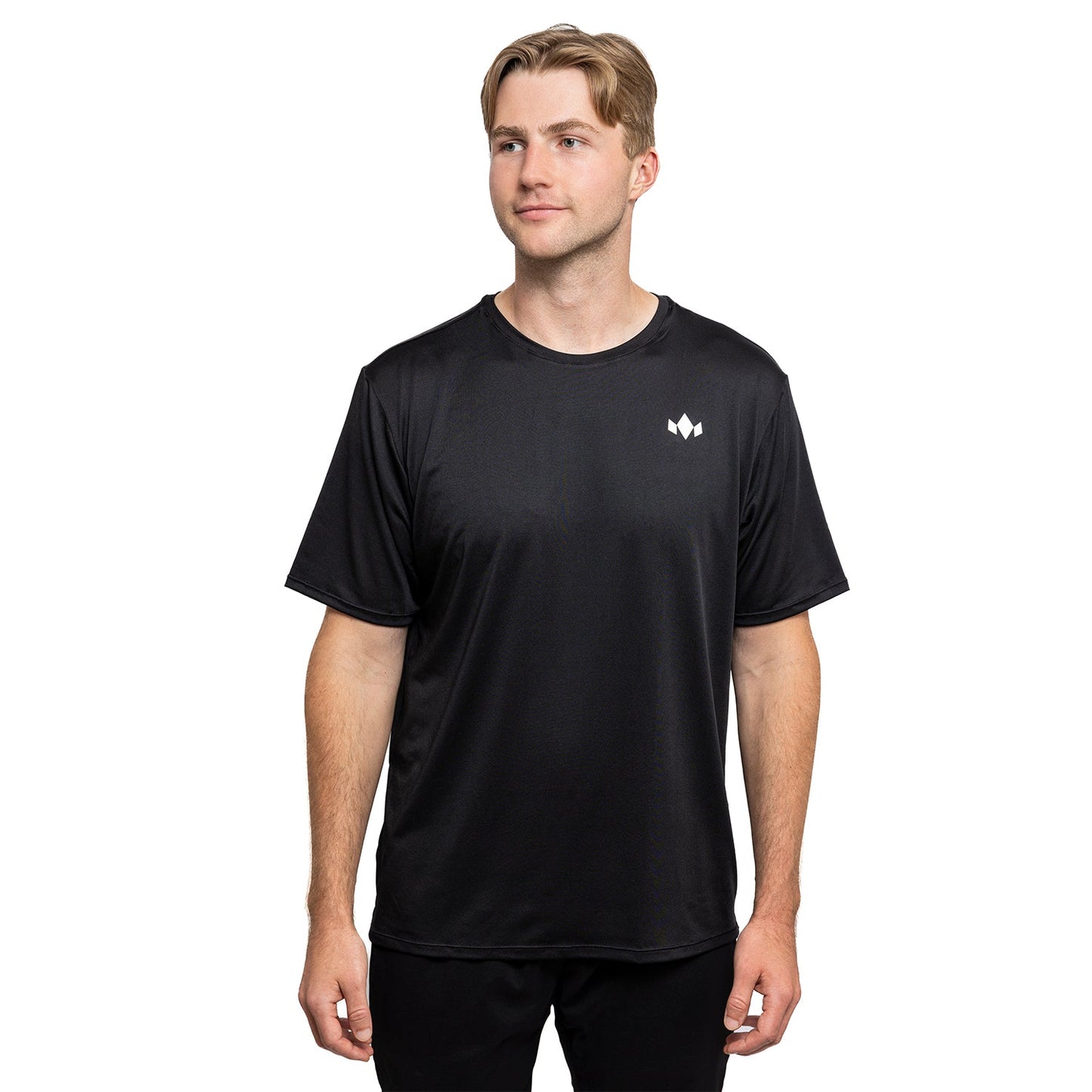 A young man with light hair wears the Diadem Sports Men's Essential Crew Neck, a loose-fitting black tee with a small white geometric logo on the left chest. He stands facing forward, smiling slightly against a white background.