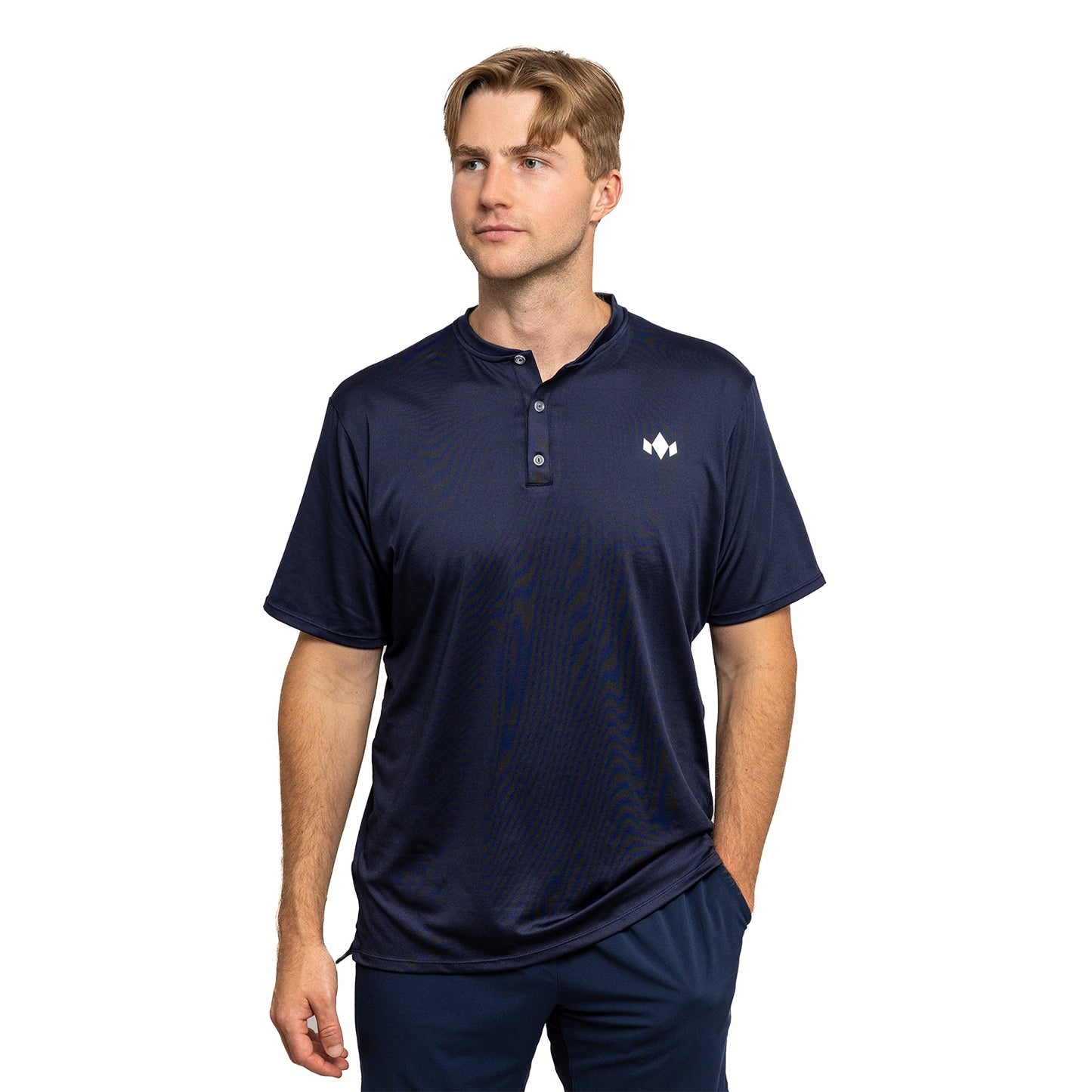 A man with light brown hair wears a navy blue Diadem Sports Men's Essential Henley with an athletic fit, three buttons, and a small white logo on the left chest, standing against a plain white background with one hand in his pocket.