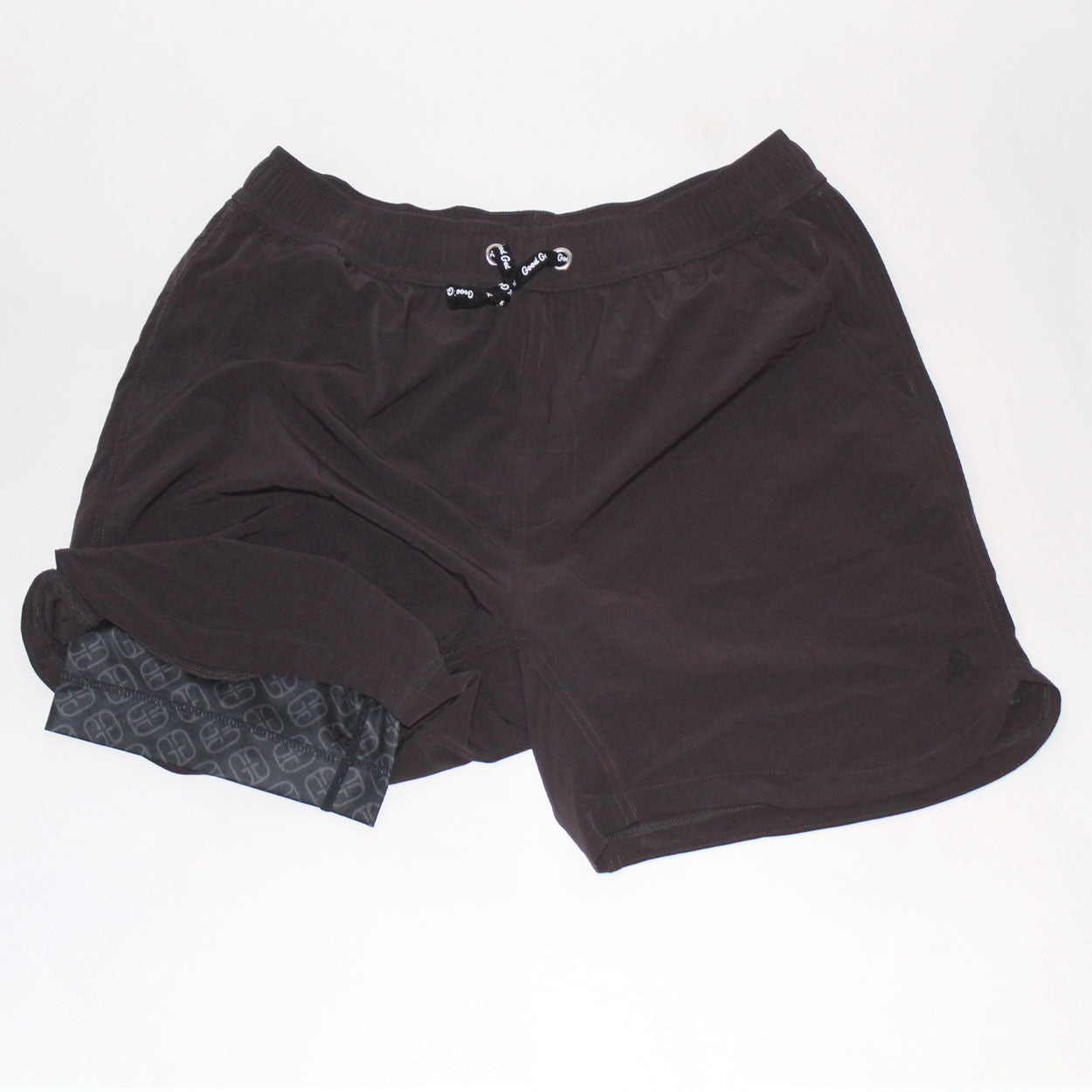 Good Get Pickleball Shorts, GG Edition, in black are laid flat on a white background. The men's shorts have an elastic waistband with drawstring, and one leg is flipped to show a black compression liner with a light geometric pattern.