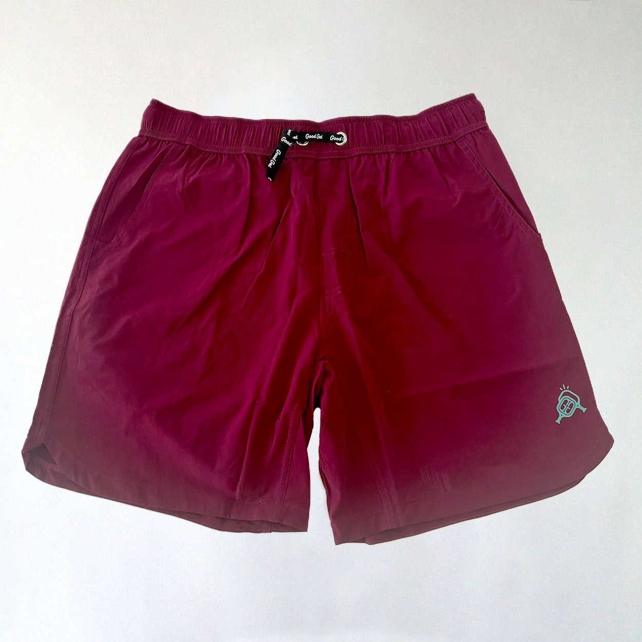 Good Get’s Magenta Me Crazy Pickleball Shorts, shown on a white background, feature lightweight magenta fabric, side pockets, an elastic waistband, and a small blue and white embroidered logo on the lower left leg.