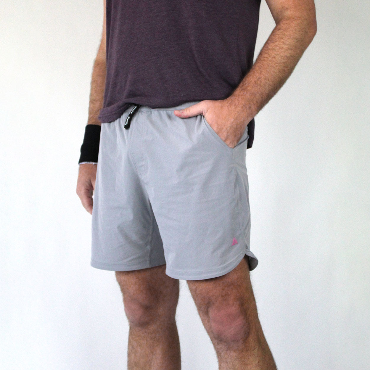 A person stands against a plain background wearing a maroon t-shirt, light gray Good Get PickleDome Edition Pickleball Shorts, and a black wristband. One hand is in the shorts pocket; only the body from shoulders to knees is visible—perfect pickleball style.