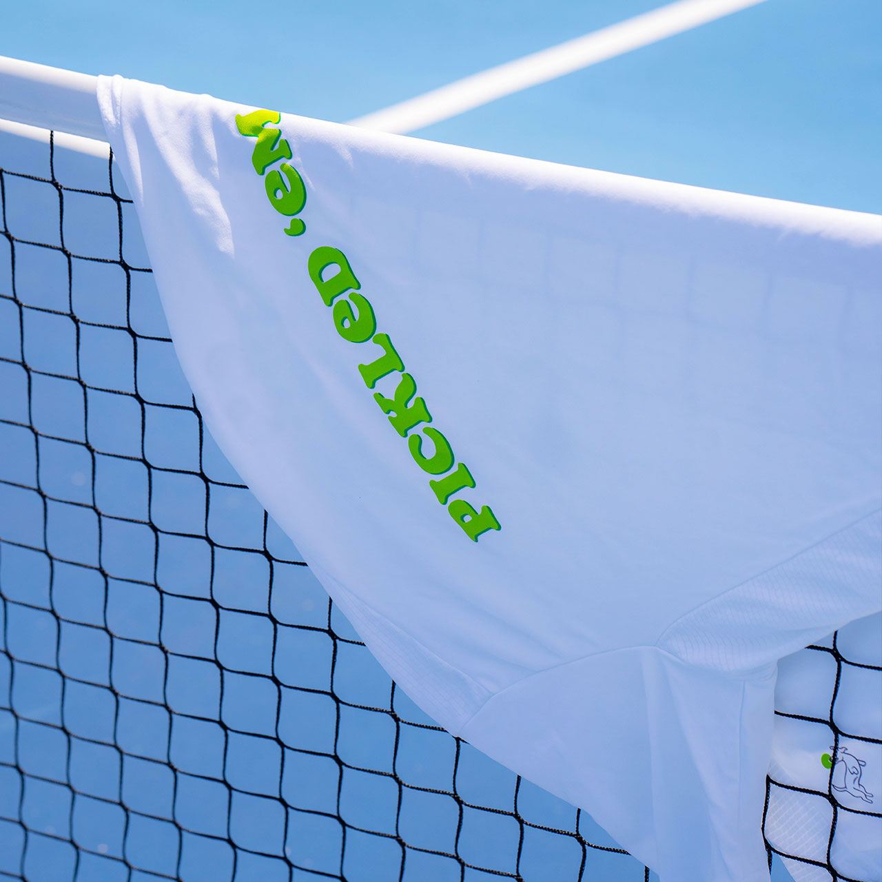 The Swinton Pickleball Men's Pickled 'Em Performance Shirt in white is displayed on a pickleball net.