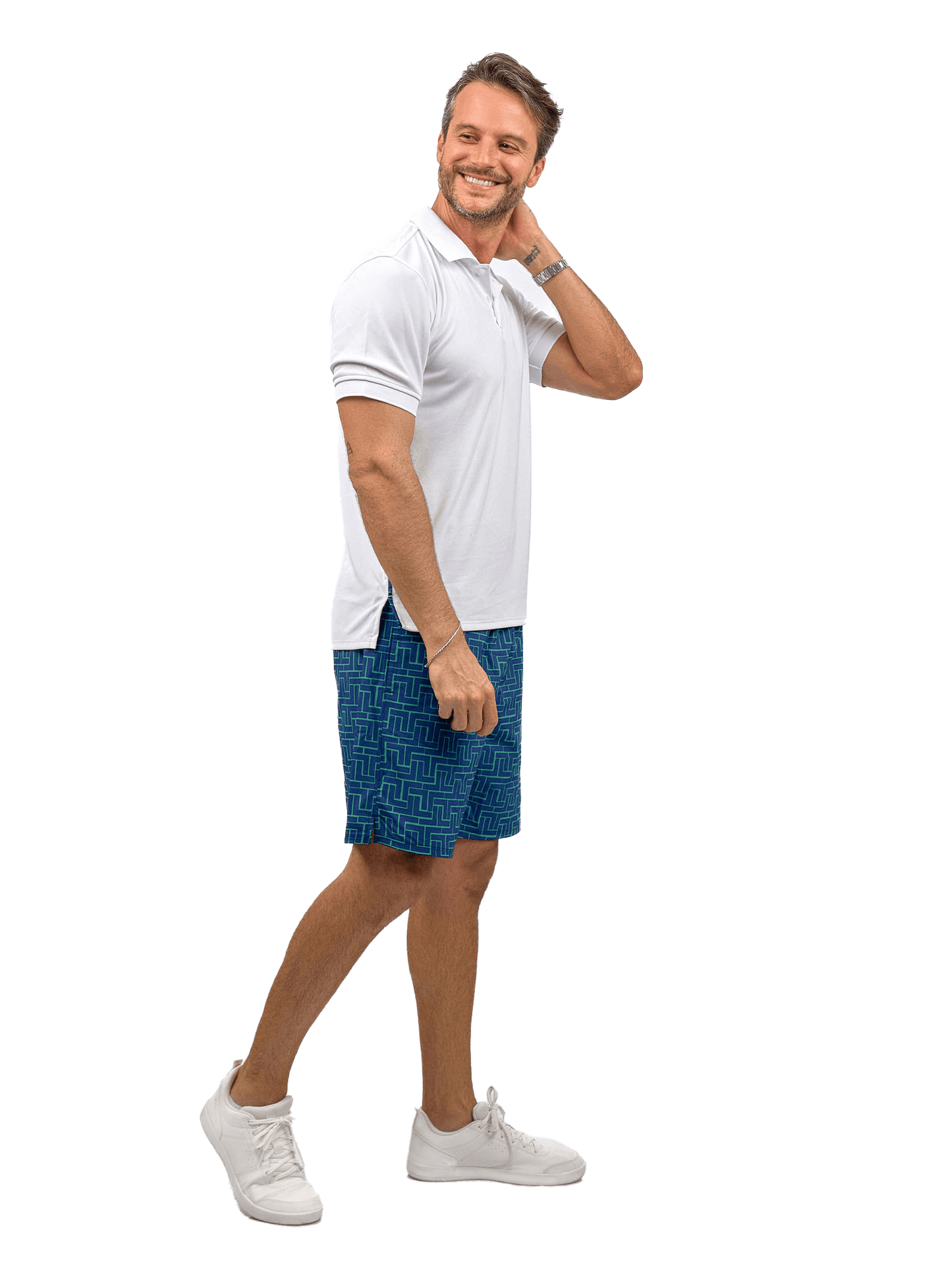 A smiling man stands against a white background, wearing the inPhorm NYC Men's Spin Polo shirt— a performance shirt for tennis & golf—along with blue patterned shorts and white sneakers, exuding a friendly, casual vibe.