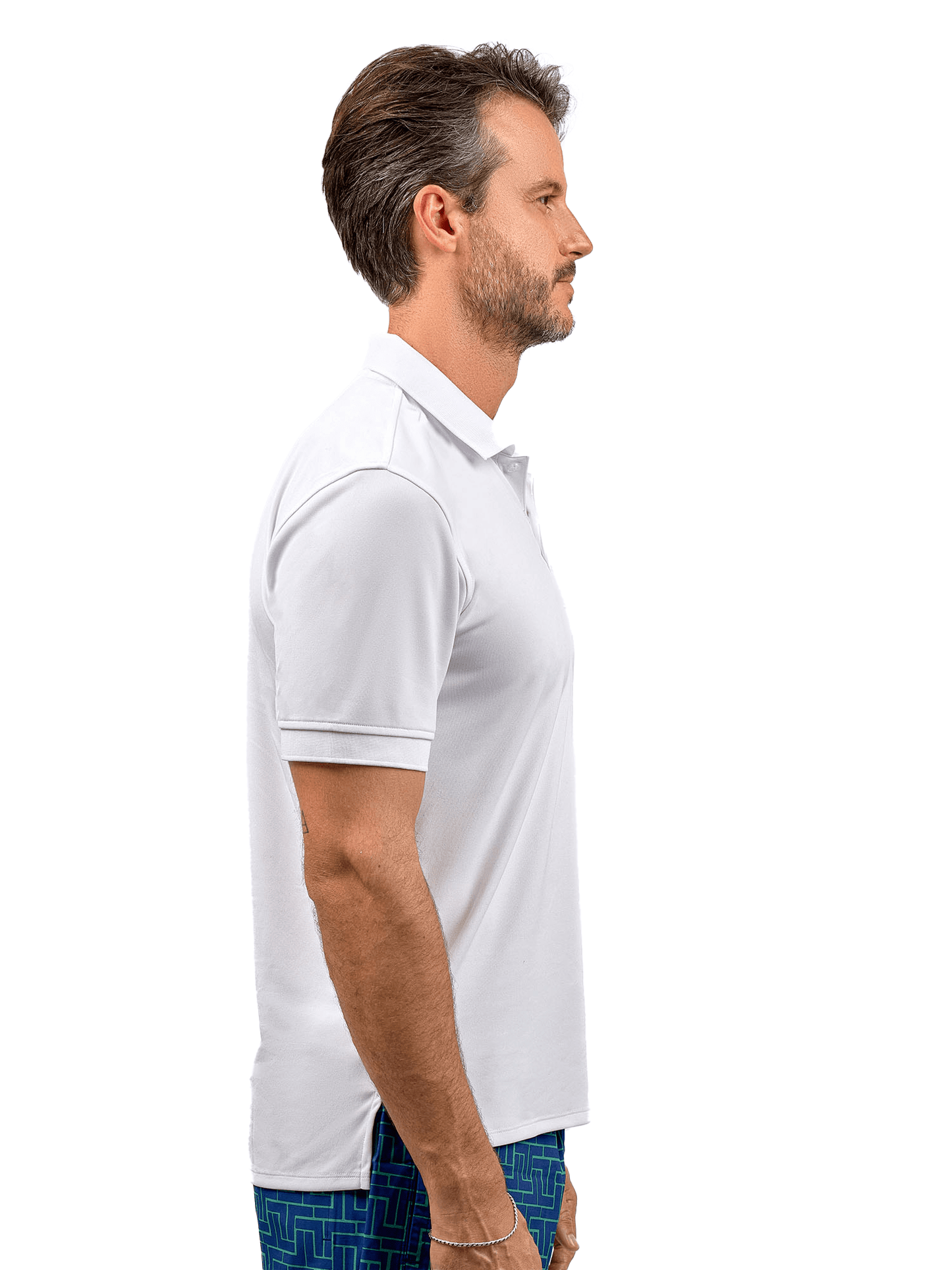 A man with short brown hair and a trimmed beard stands in profile facing right, wearing the inPhorm NYC Men's Spin Polo shirt—Performance Shirt for Tennis & Golf—with patterned blue shorts against a plain white background.