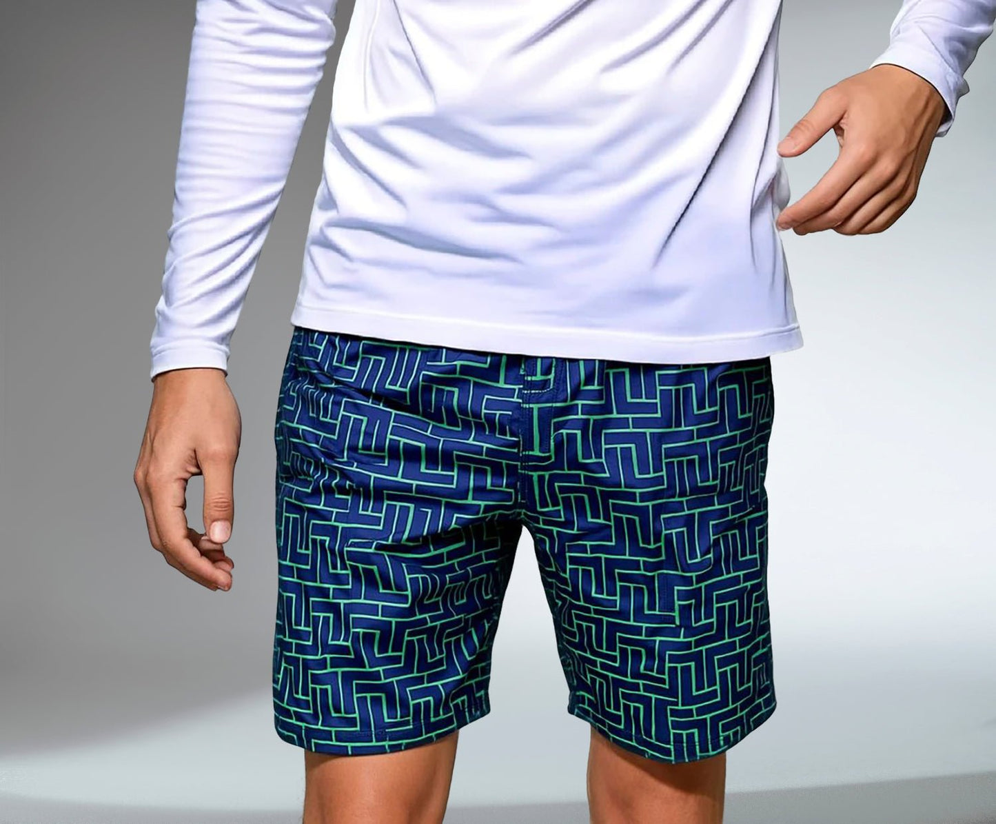 A person wears a long-sleeve white shirt and inPhorm NYC Men's Tennis Shorts - Spin Shorts with Pockets & UV Protection - Tessel, featuring a blue base and green geometric pattern; only the torso and upper legs are shown on a gray background.