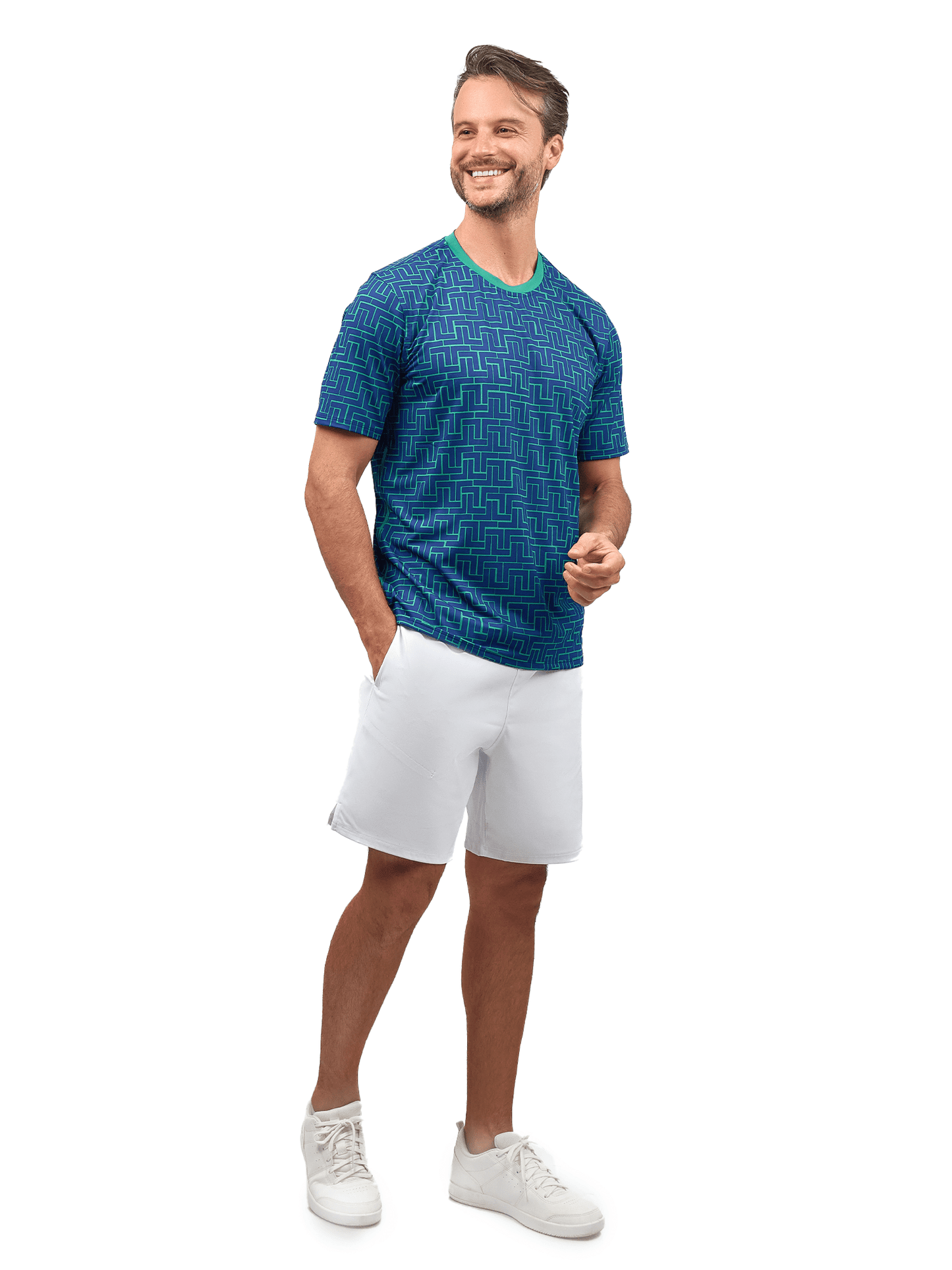 A man with short hair and a trimmed beard smiles, wearing inPhorm NYC's Men's Spin Tennis Shorts with Pockets & UV Protection in white, along with a blue patterned shirt and white sneakers. His left hand rests in his pocket, set against a plain white background.