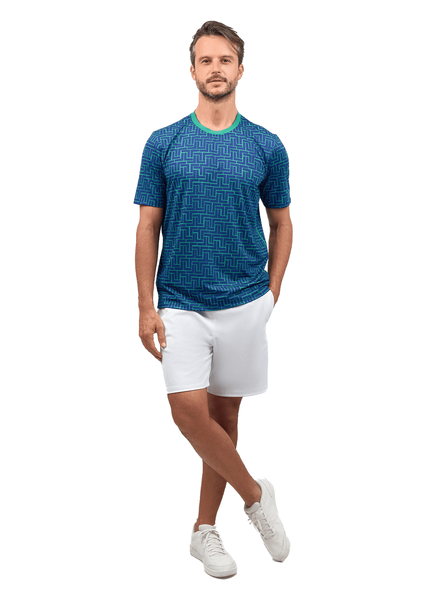 A man stands facing forward, left hand in his pocket, wearing inPhorm NYC Men's Tennis Shorts - Spin Shorts with Pockets & UV Protection in white against a plain white background. He pairs them with a blue patterned shirt and white sneakers.
