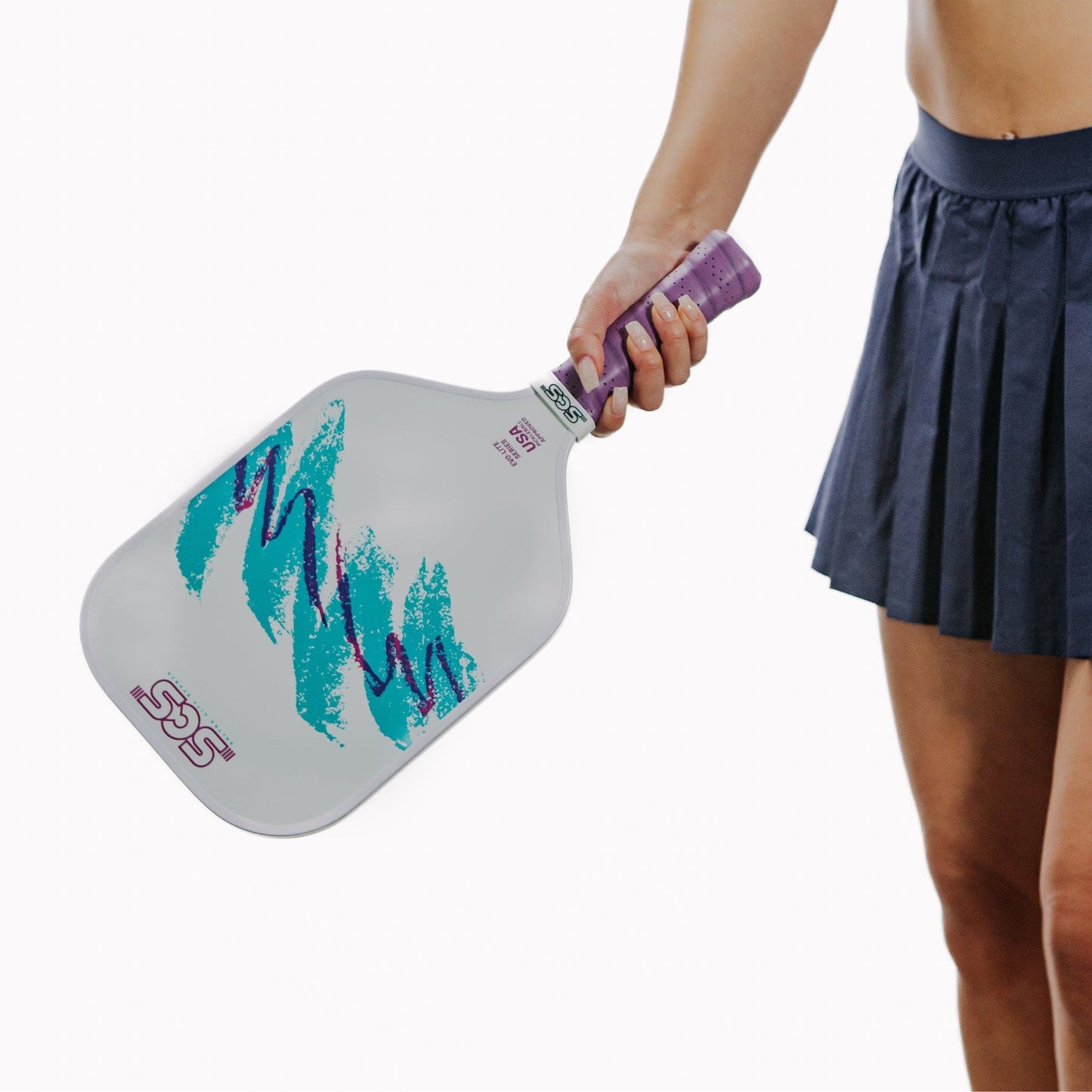 A person in a navy pleated skirt holds the Salted City Sports Nostalgia | Evo-Lite Series pickleball paddle, featuring a white face with teal and purple brushstroke designs and a purple grip. The handle is wrapped in purple tape. Background is plain white.