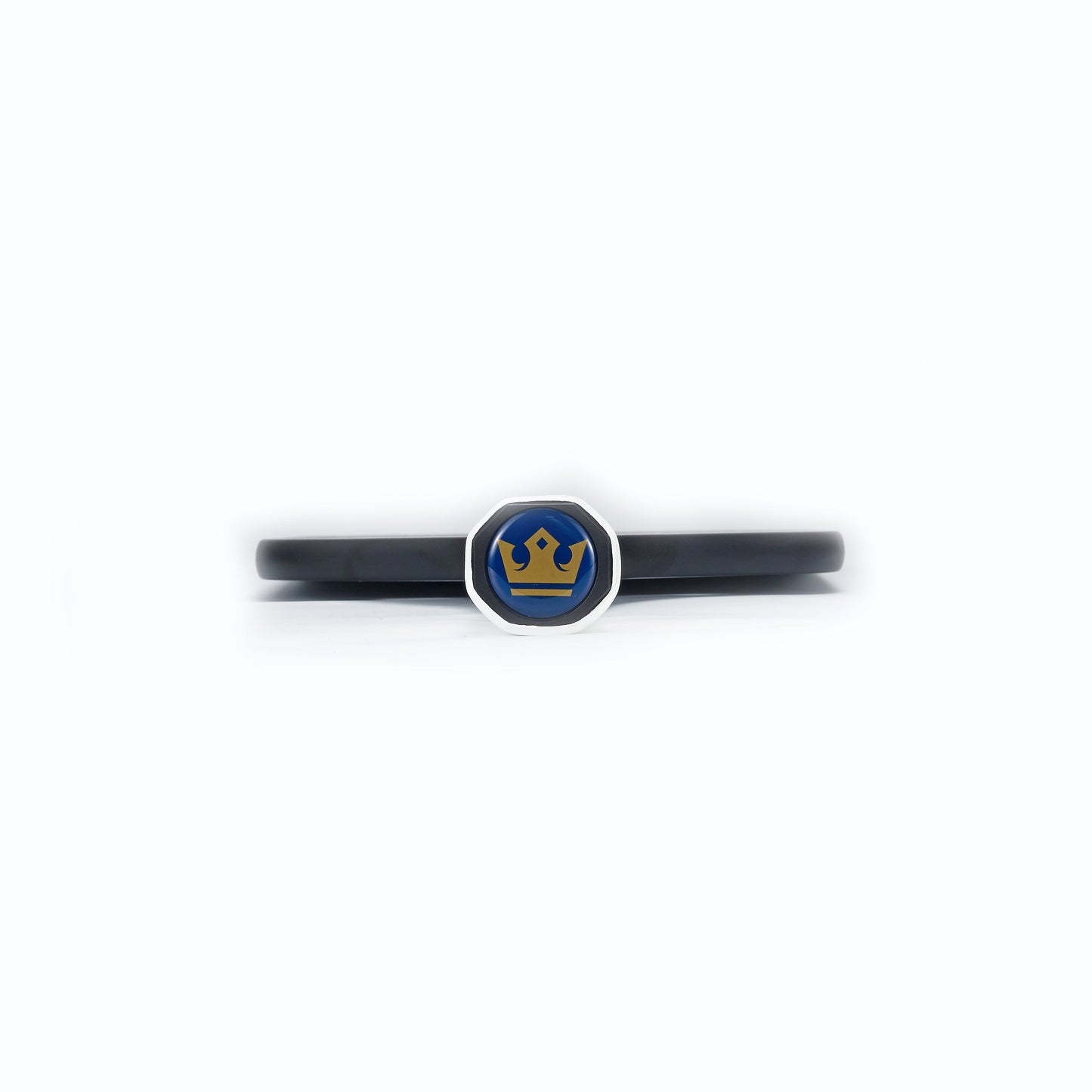 The ARTI Carbon Fiber "MASTERY ELITE 1.0" Paddle wristband features a black band with a round, silver-edged centerpiece, blue background, and yellow crown icon—a stylish accessory for ARTI pickleball paddle fans. Displayed on a plain white background.