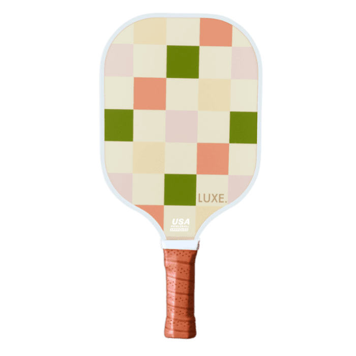 The Party Checker by LUXE Pickleball is a fiberglass paddle with a brown leather-wrapped handle and green, peach, blush pink, cream, and coral checkerboard face. It features a honeycomb polymer core and USA Pickleball Approved logo near the handle. White background.