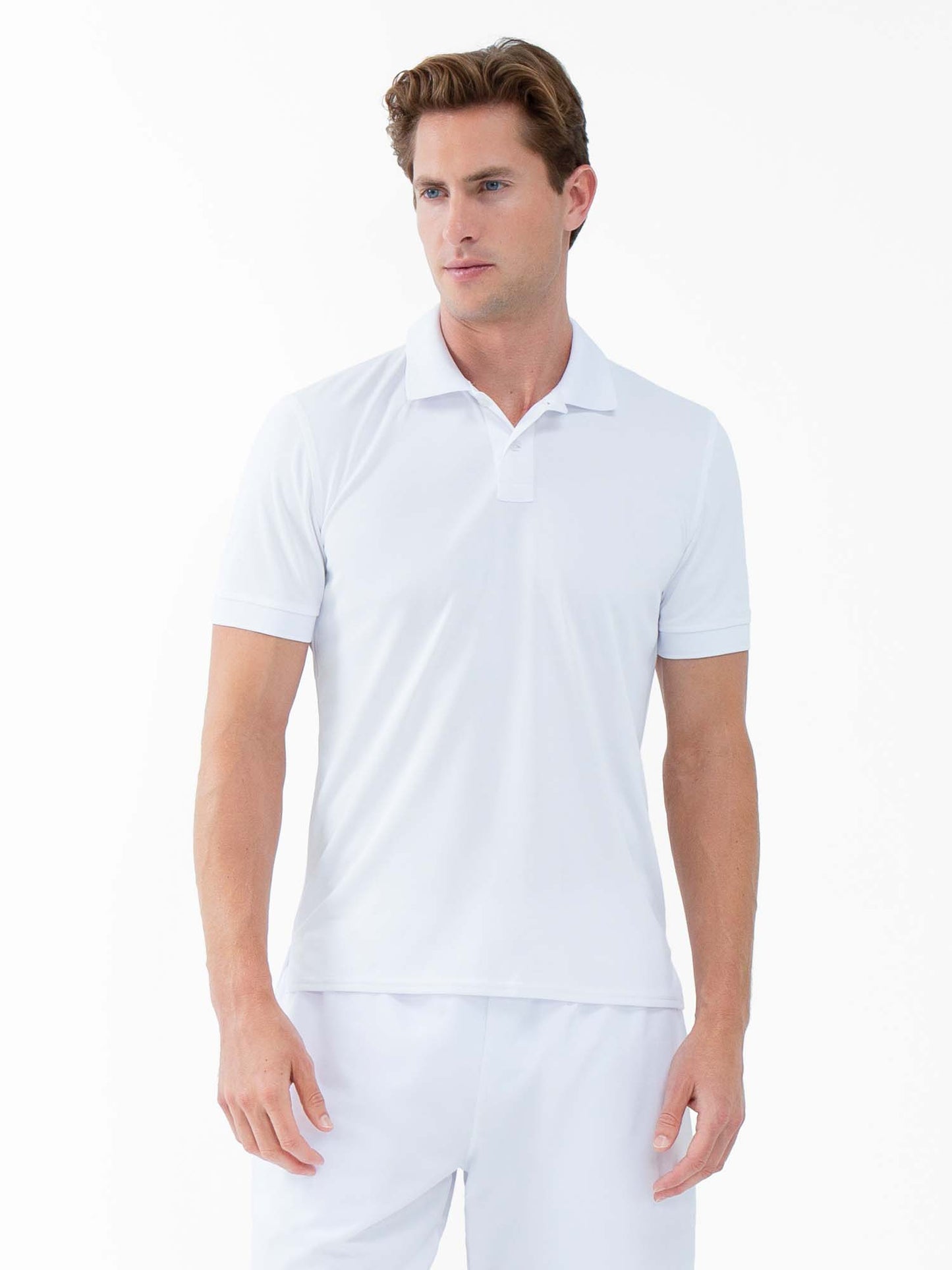 A man with light skin and short brown hair stands against a plain white background, wearing the inPhorm NYC Performance Men's Classic Tennis Rib Collar Polo in white, showcasing its moisture-wicking comfort and classic style.