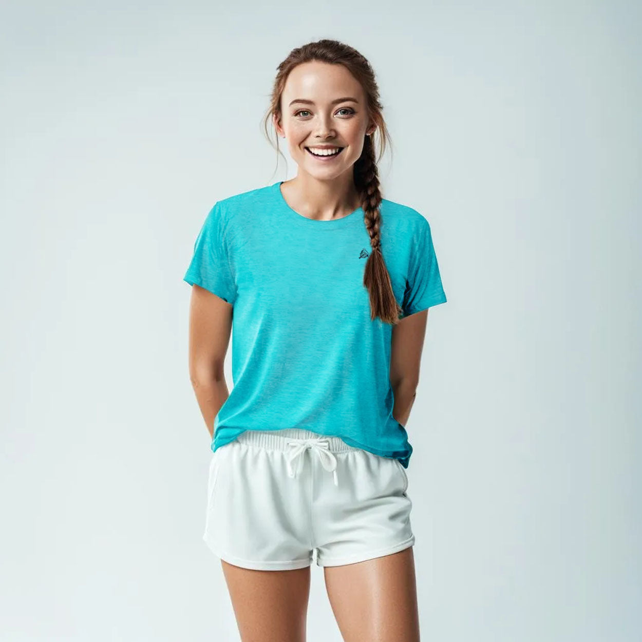A young woman with light skin and long brown hair in a braid smiles at the camera, wearing the Good Get AeroBliss Performance Short Sleeve T-shirt in bright blue and white shorts, standing against a plain light gray background.