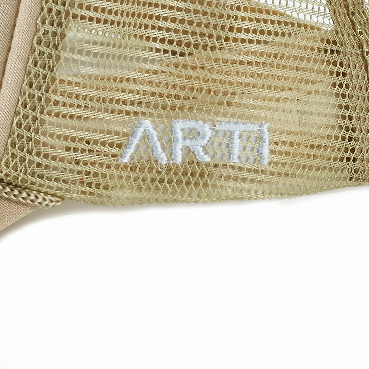 Close-up of beige mesh fabric from the ARTI Pickle Me Trucker Hat, featuring partially visible white ARTI embroidery. The fine mesh overlays a solid layer, highlighting the hat's sporty and stylish design.