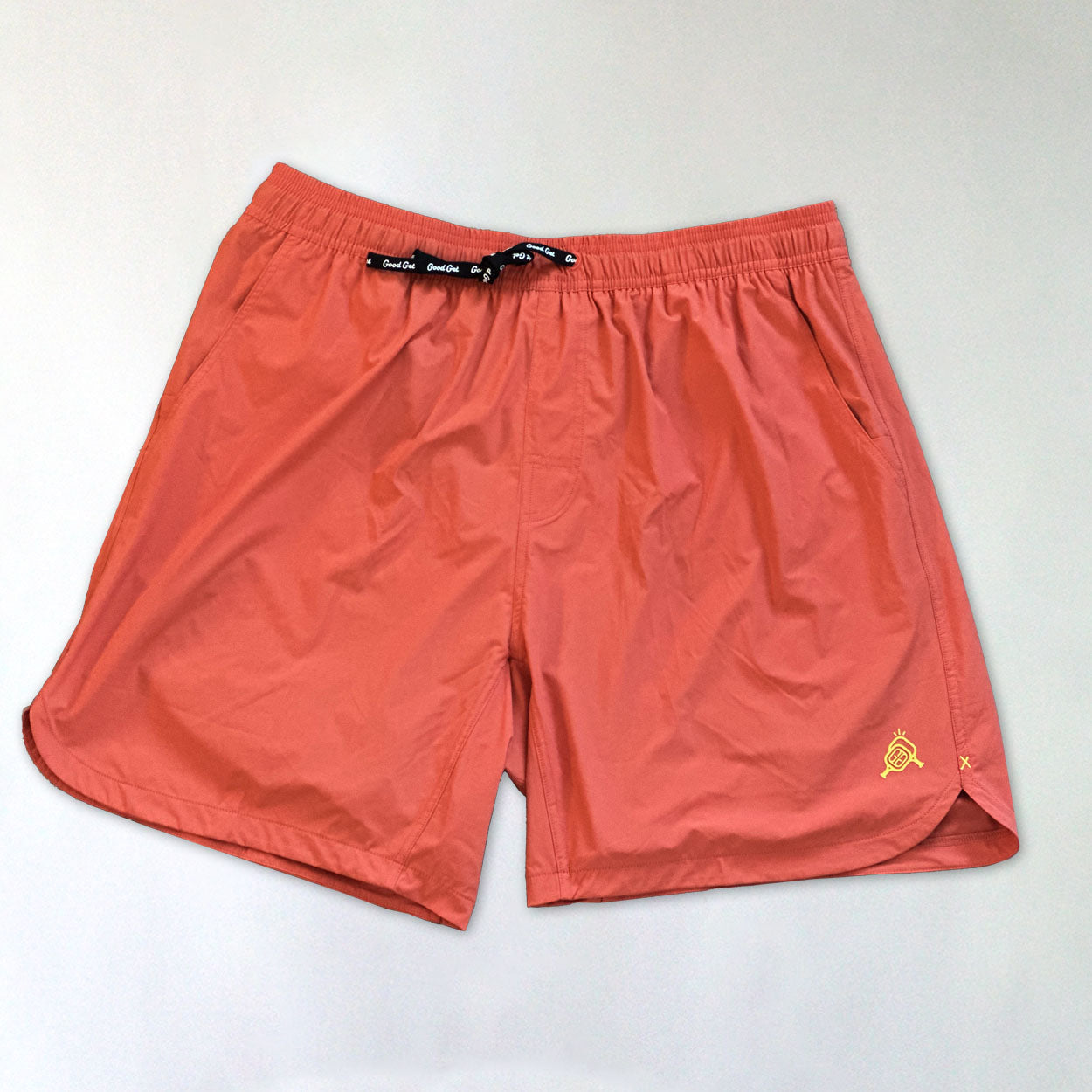 Good Get Pickleball Shorts, Drippy Edition, in coral with an elastic waistband, black drawstring, subtle yellow logo embroidery, small side slit, and 6-way stretch—perfect for sports or casual wear.