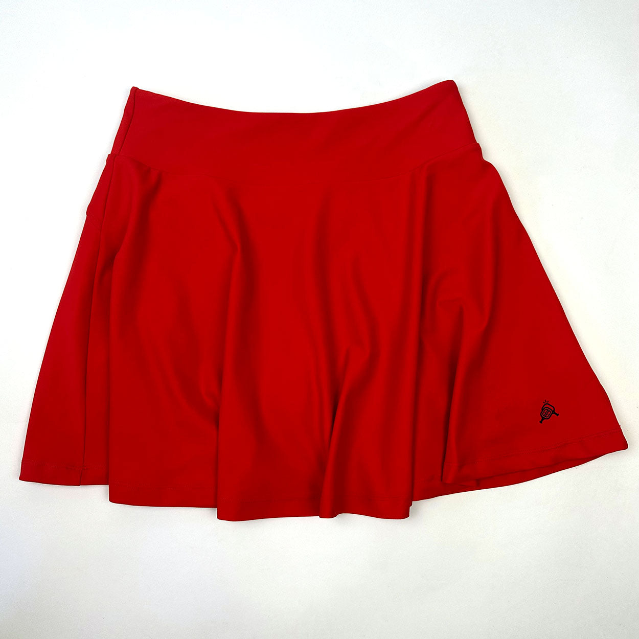 The Good Get Skirtin' Round the Kitchen - Rally Red Edition is a bright red, knee-length pickleball skirt with a wide waistband, smooth moisture-wicking fabric, and a small black logo near the right hem. Plain white background.